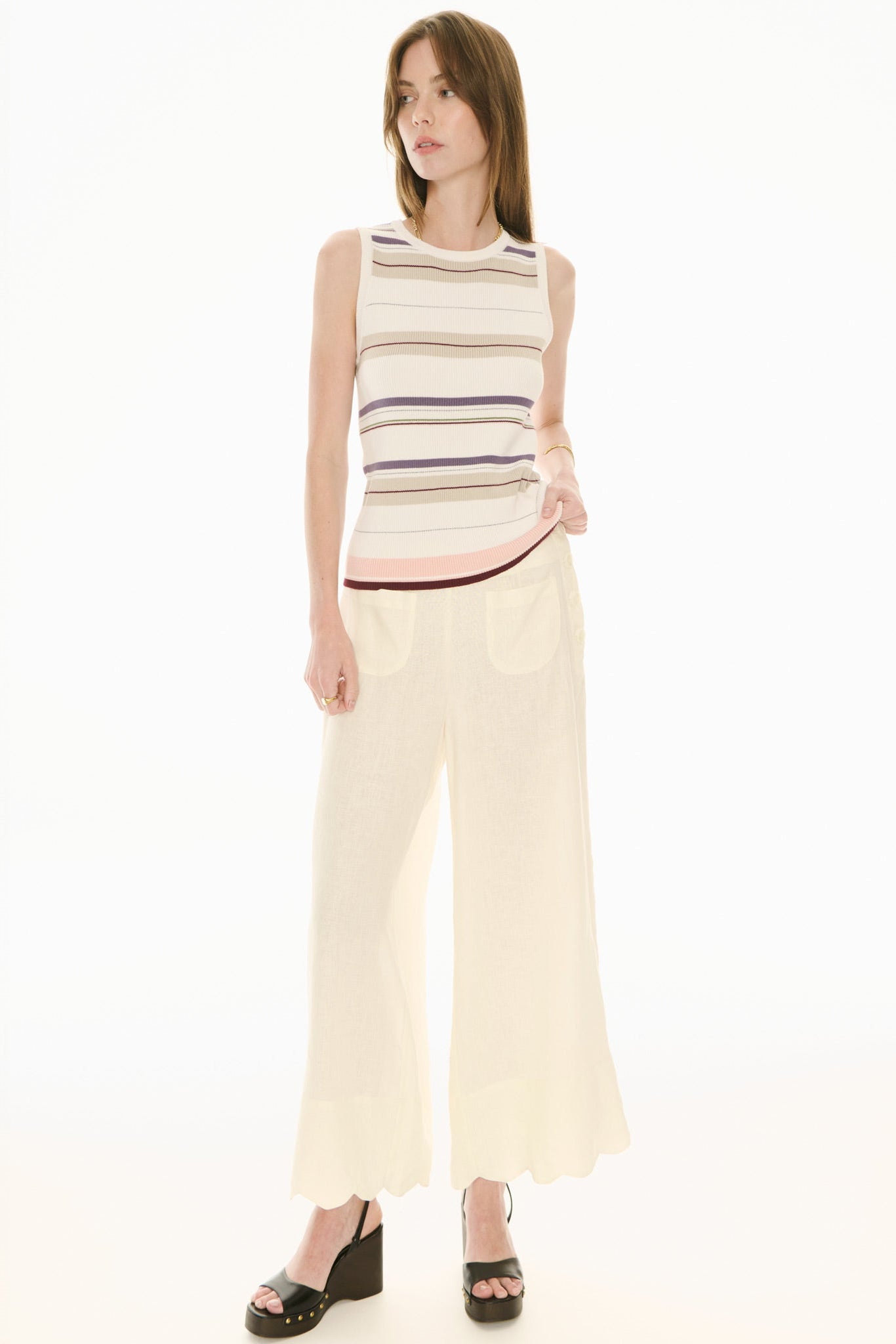 Woman wearing a sleeveless striped top and cream pants on a white background