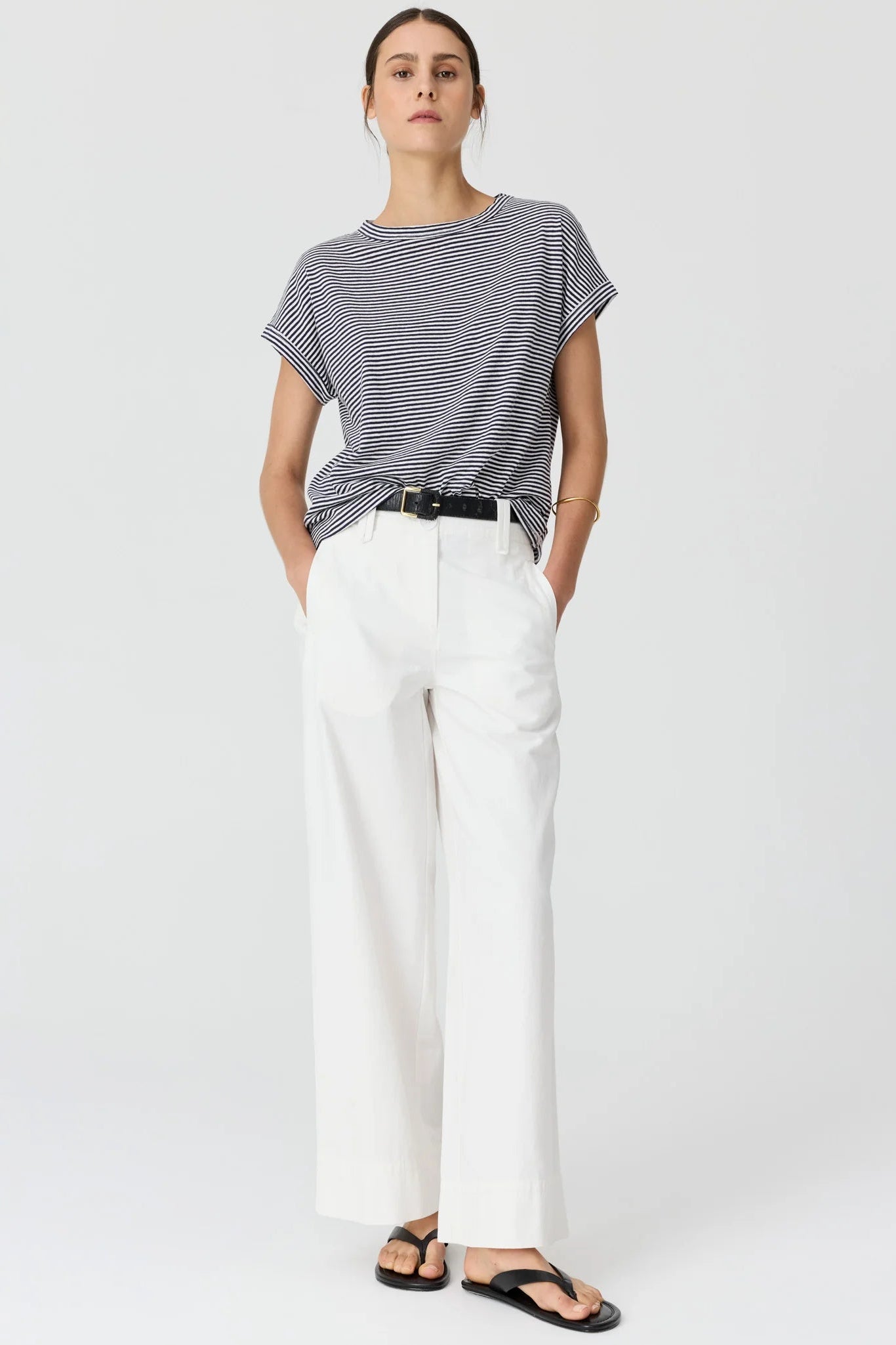 Model with her hair tied back wearing a navy and white stripe short sleeve tee and white wide leg pants and sandals. 