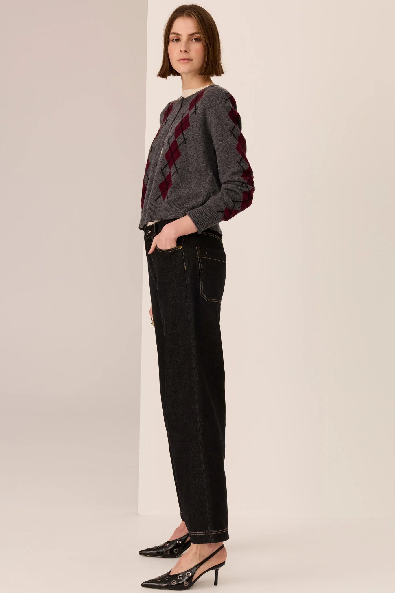 Person wearing a gray sweater with red diamond patterns and black pants on a beige background
