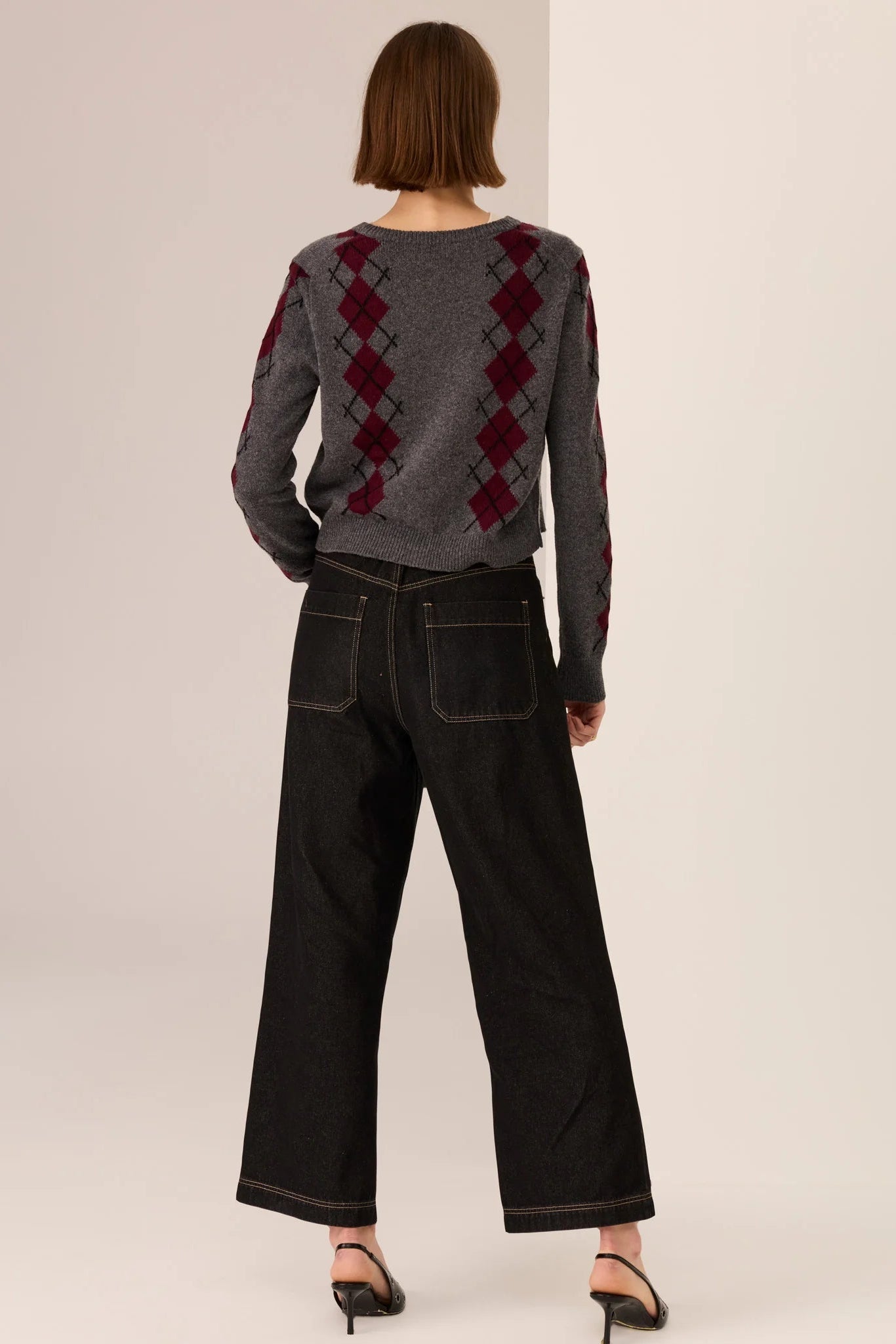 Person wearing a gray sweater with red diamond pattern and black pants on a white background