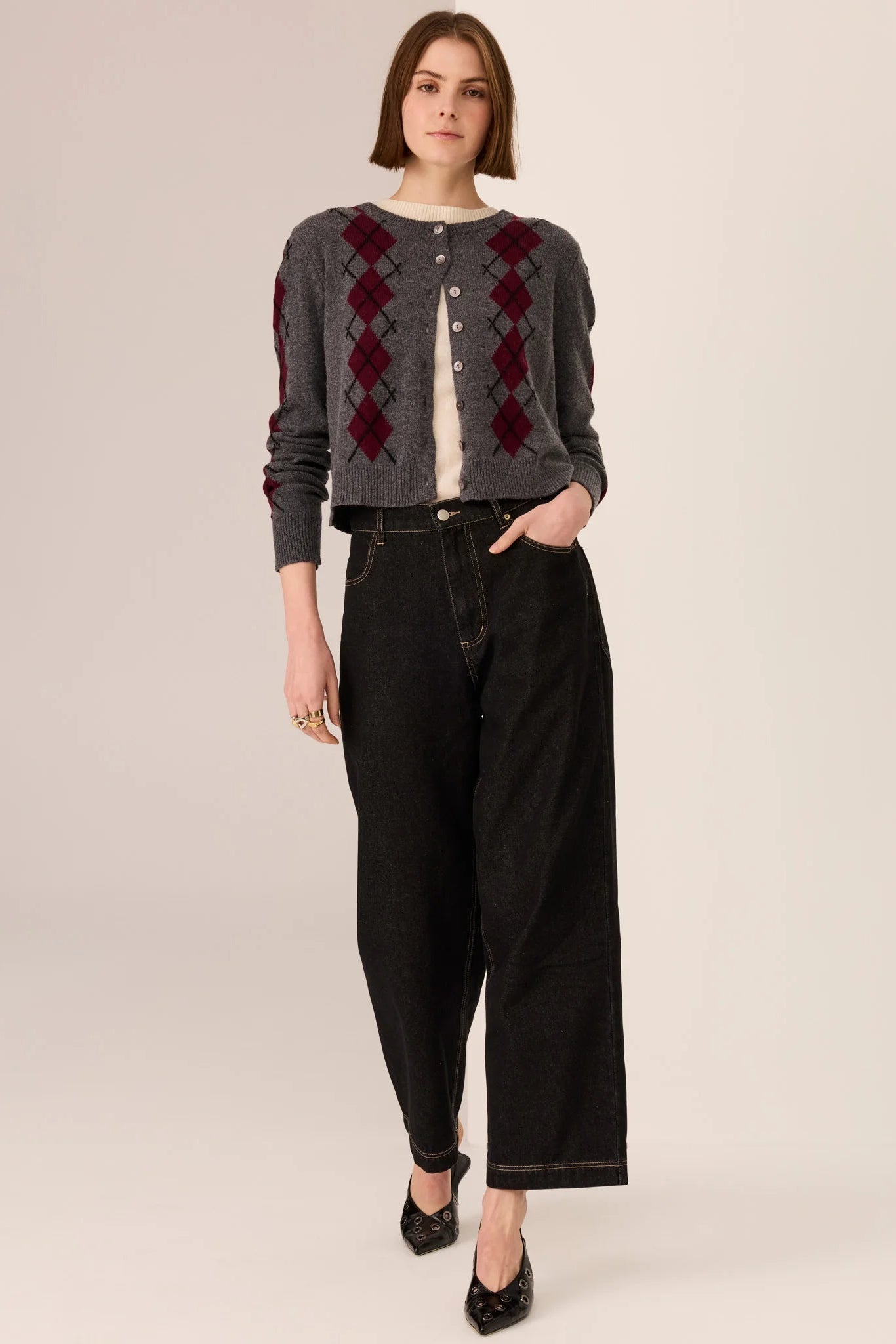 Woman wearing a patterned cardigan and black pants on a plain background