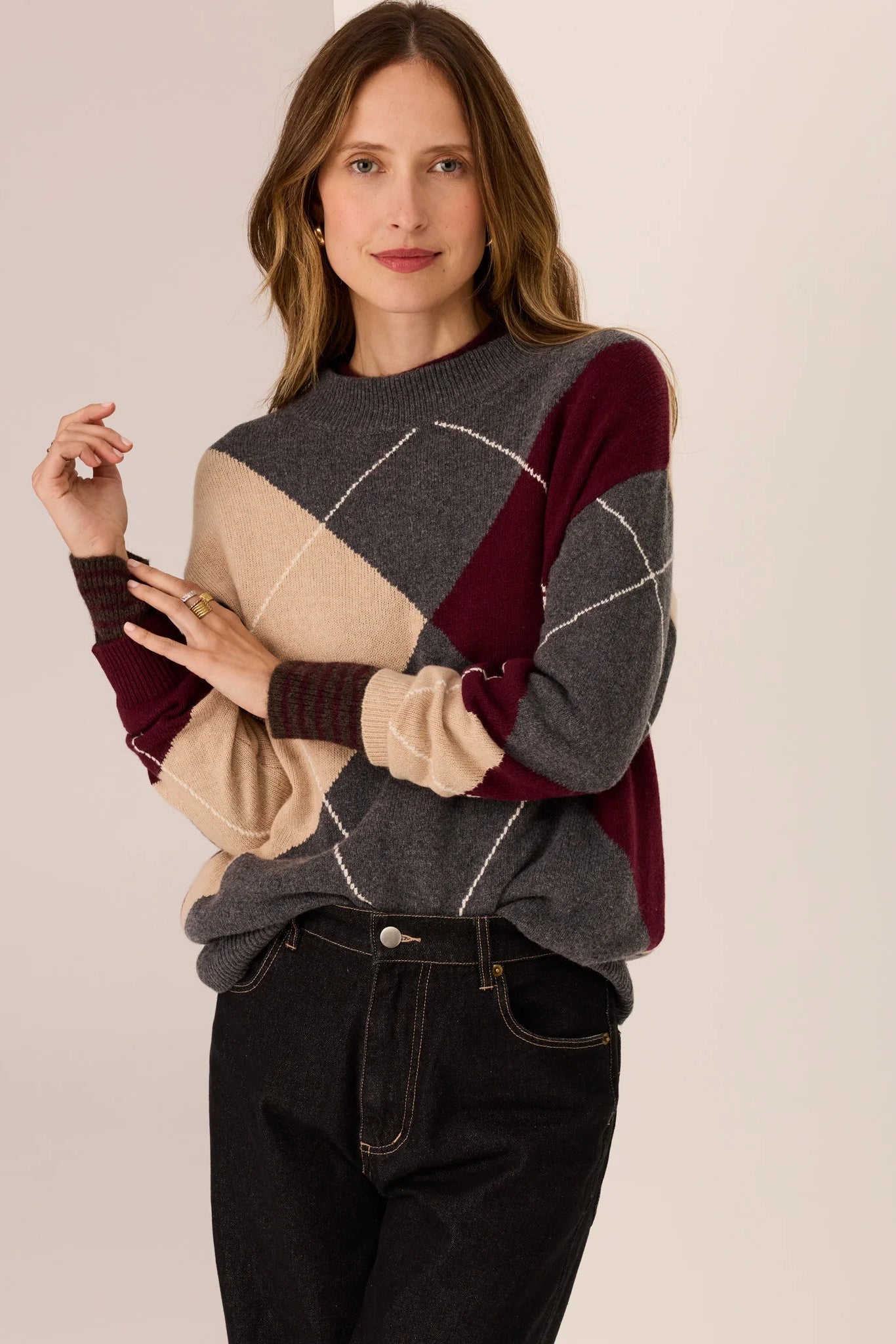 Woman wearing a color-blocked sweater with maroon, beige, and gray sections on a plain background.