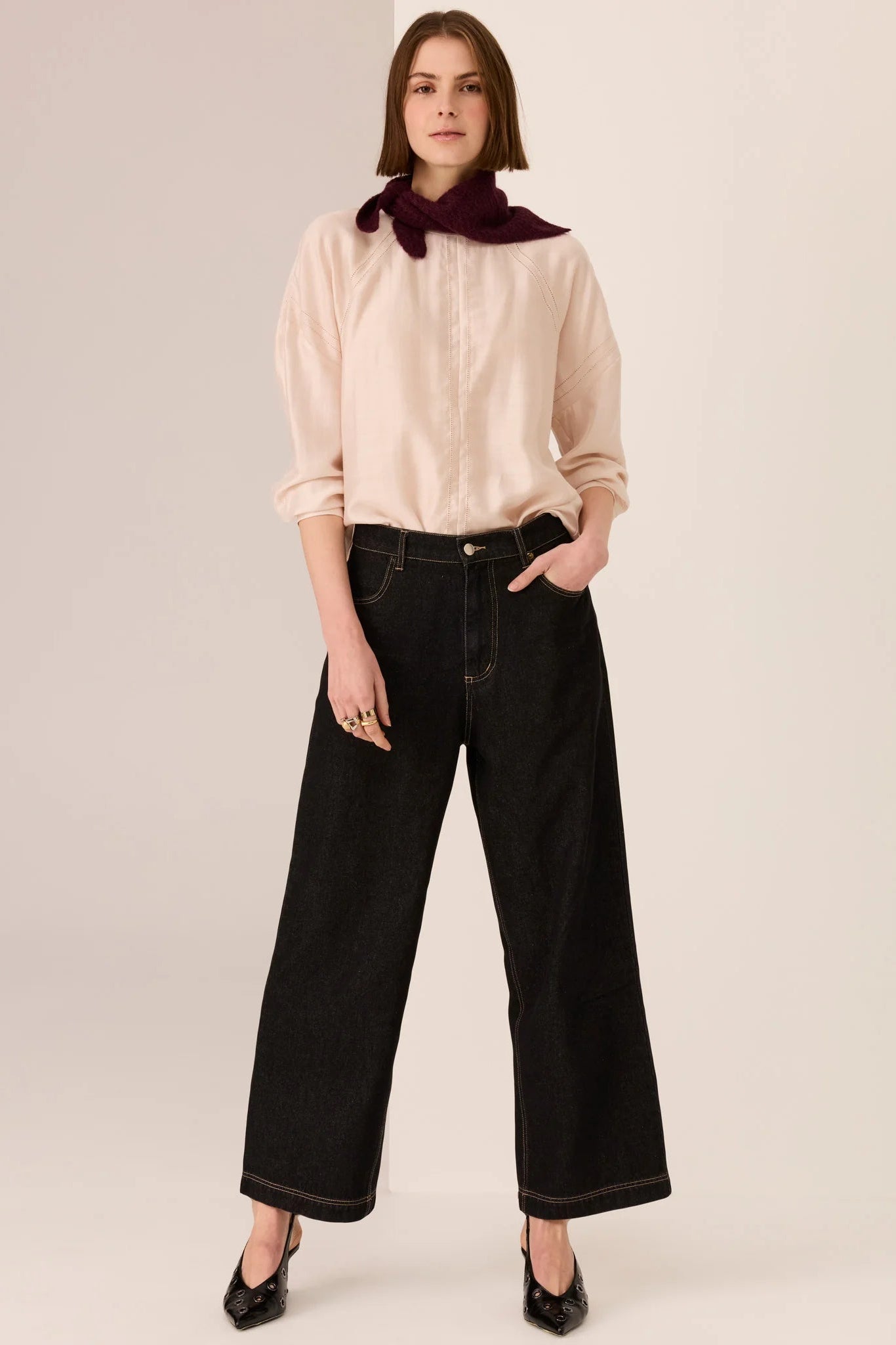 Woman wearing a beige blouse and black pants with a red scarf on a white background