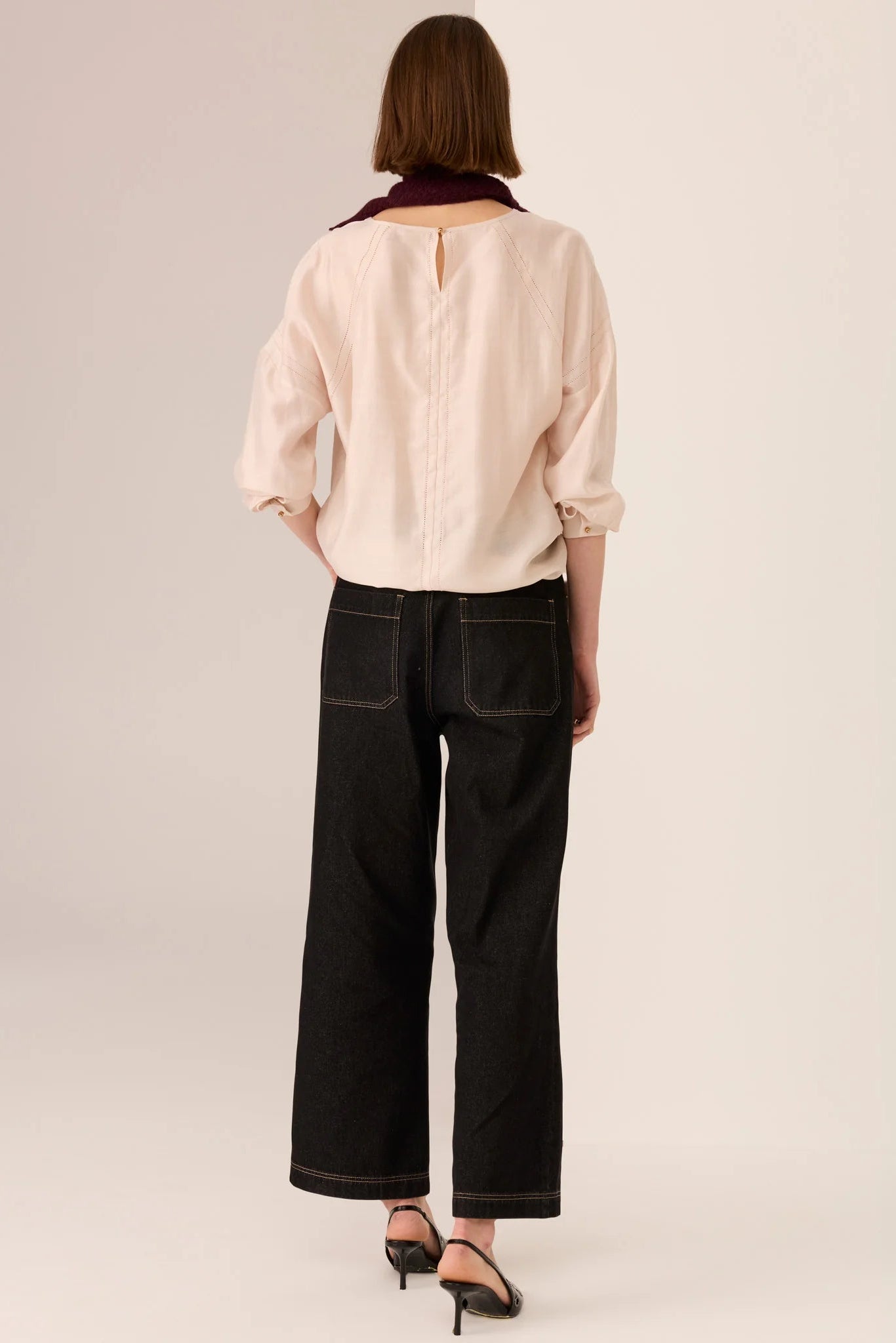 Person wearing a light pink blouse and black pants on a beige background