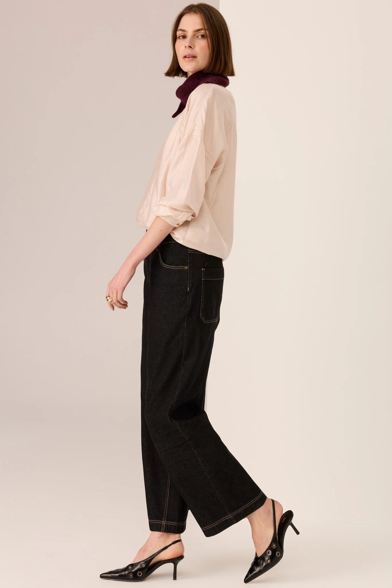 Woman wearing a beige blouse and black pants on a plain background