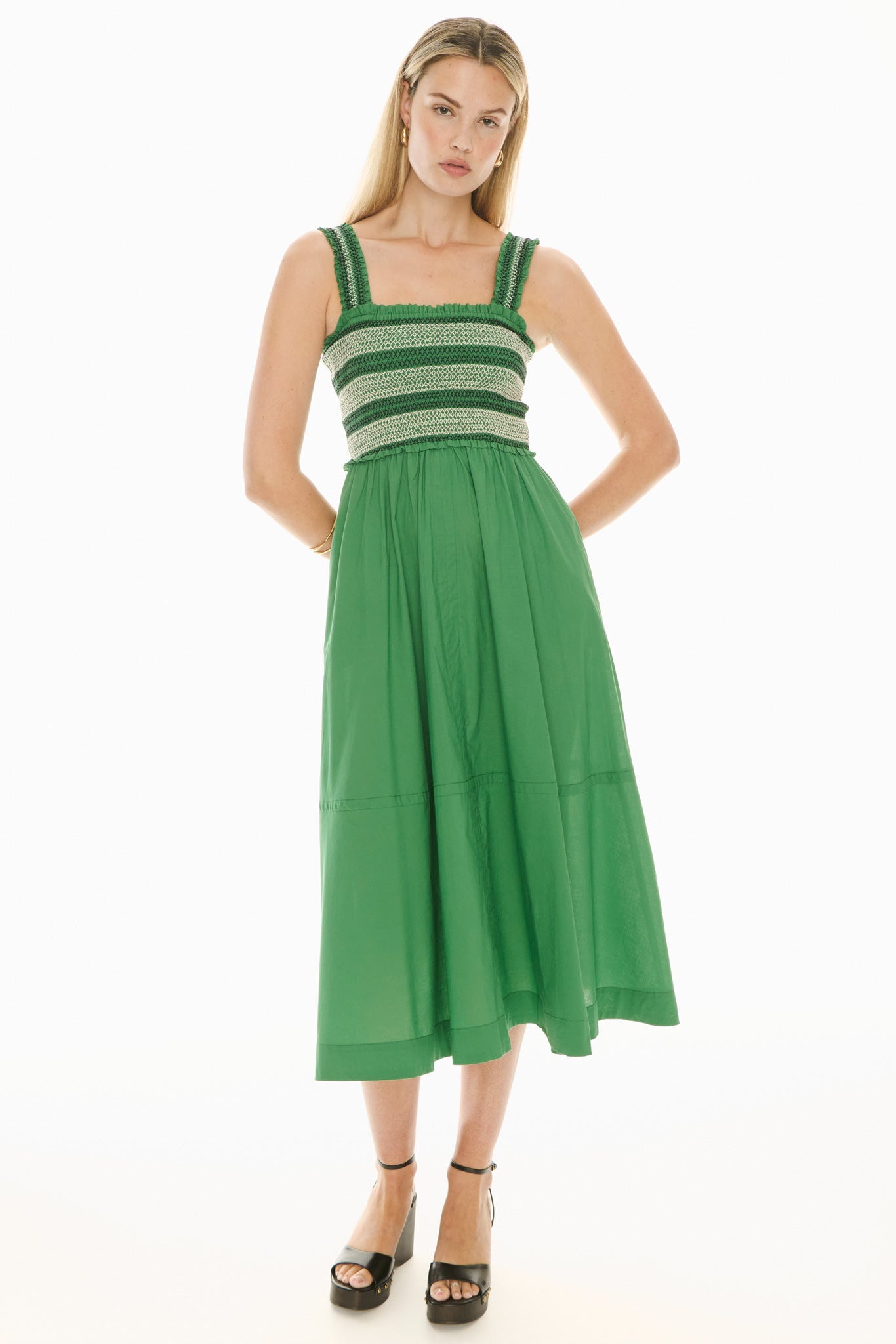 Model wearing a green and white sundress with smoked bodice on a white background. 