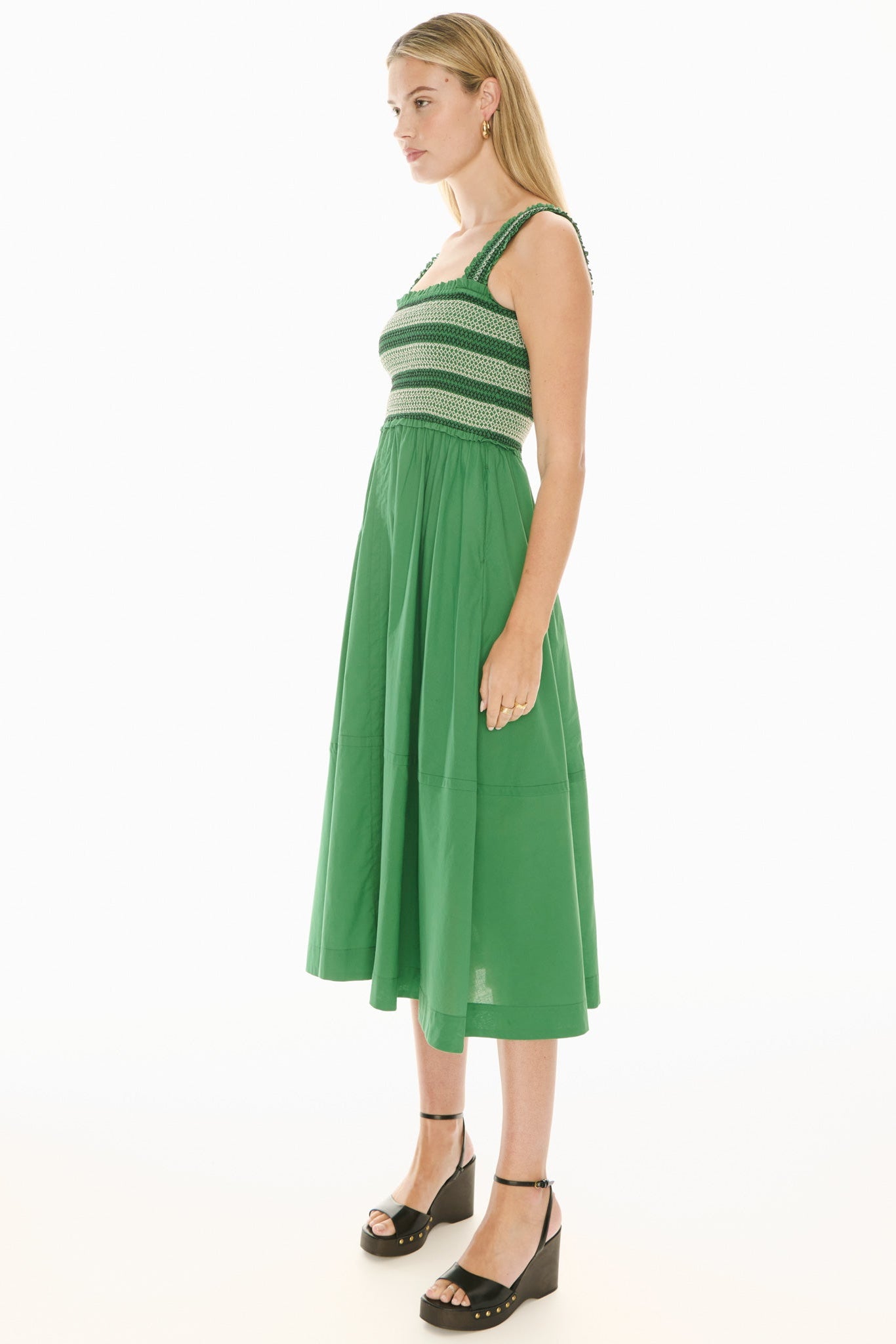 Model wearing a green and white sundress with smoked bodice on a white background. 
