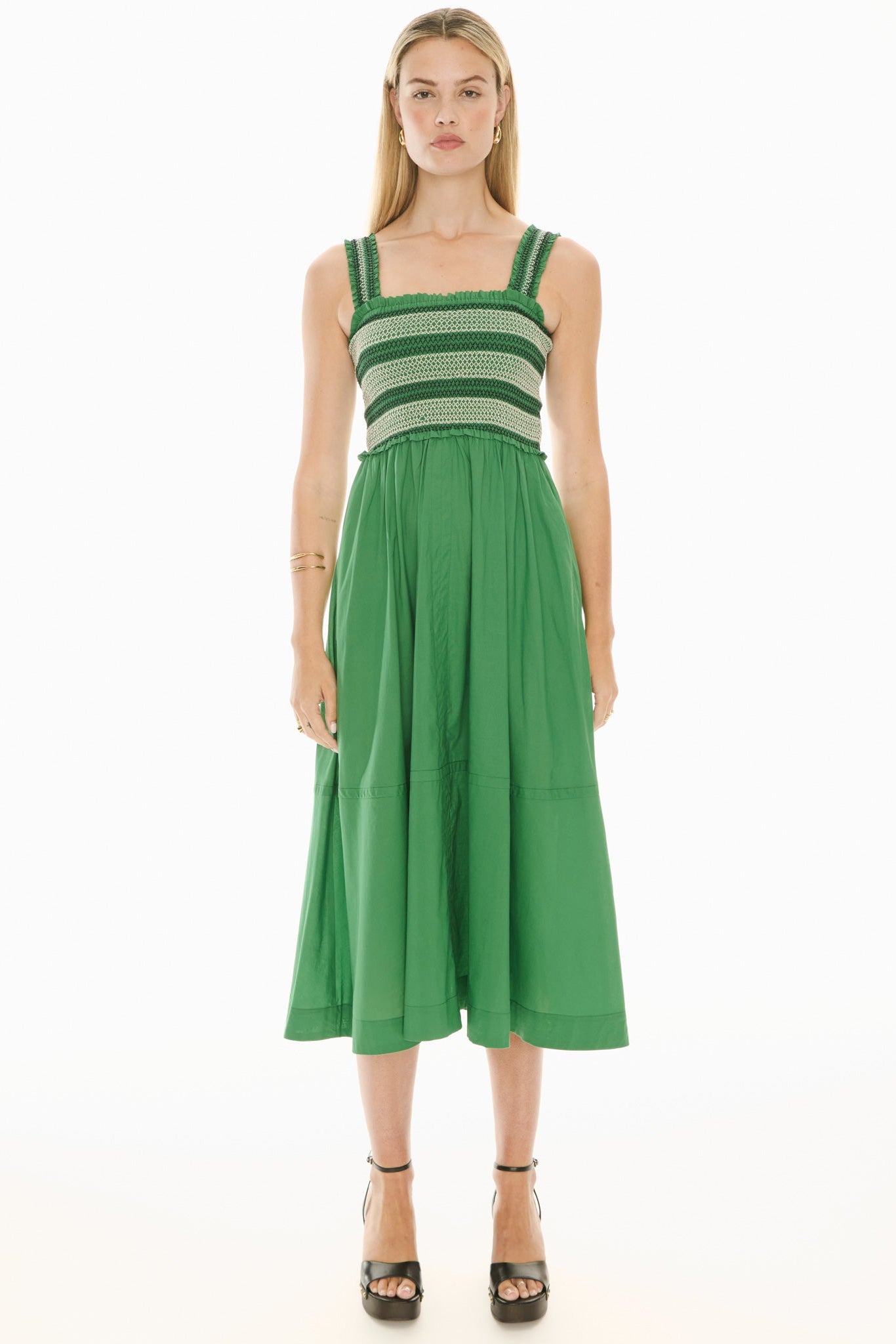 Model wearing a green and white sundress with smoked bodice on a white background.  