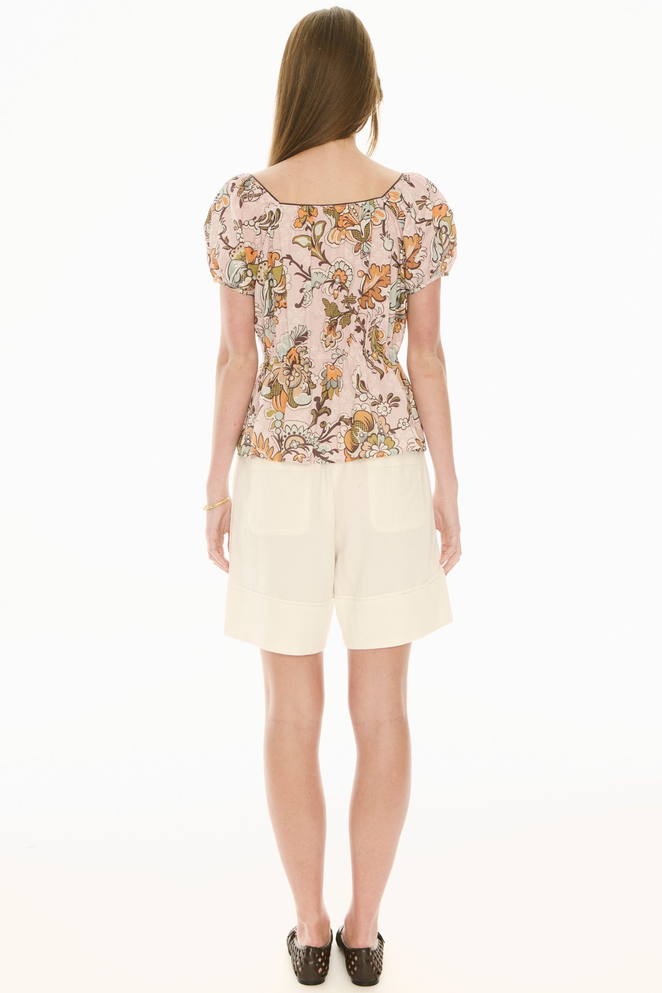 Woman wearing a floral top and ecru white shorts on a white background