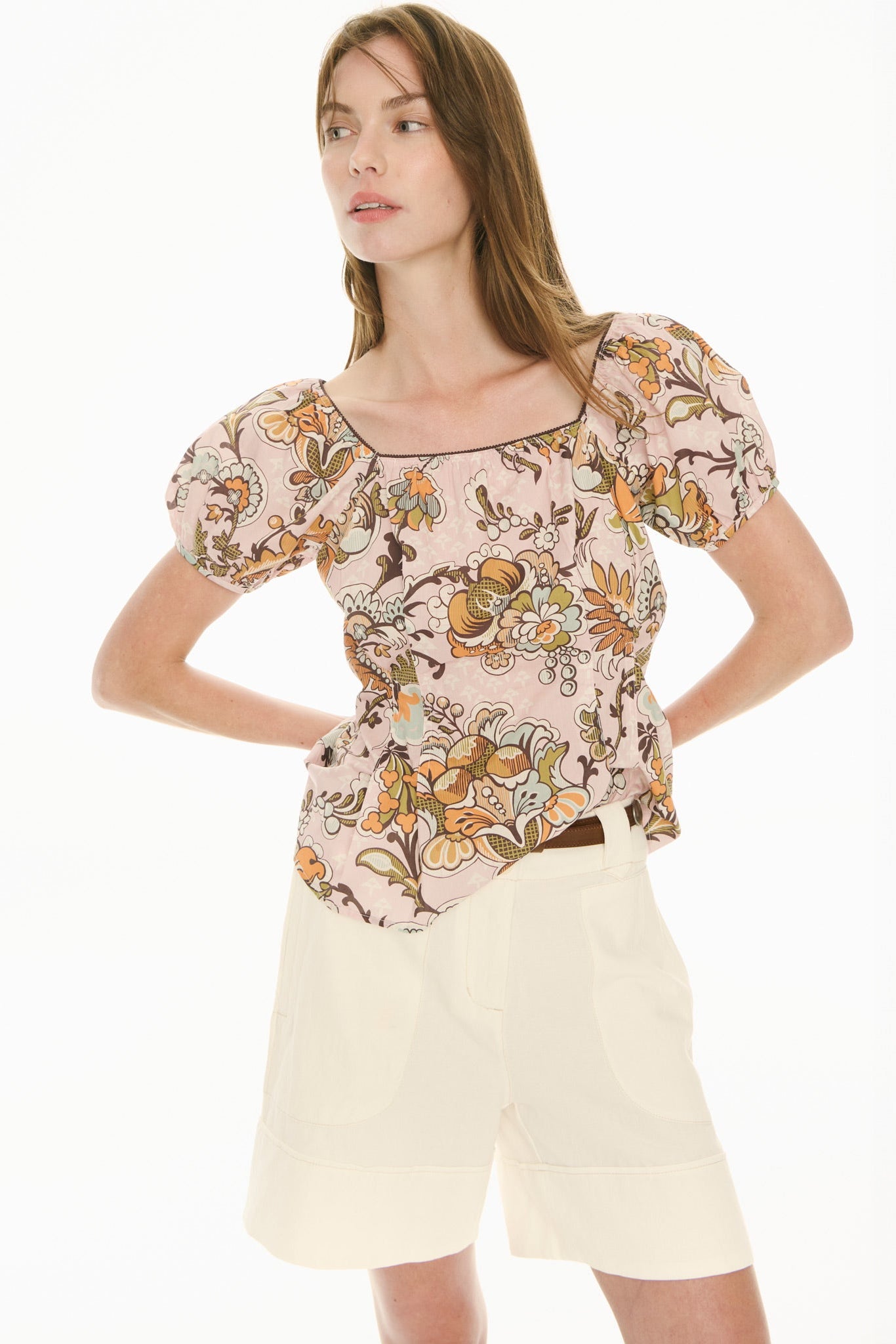 Woman wearing a floral top and ecru white shorts on a white background