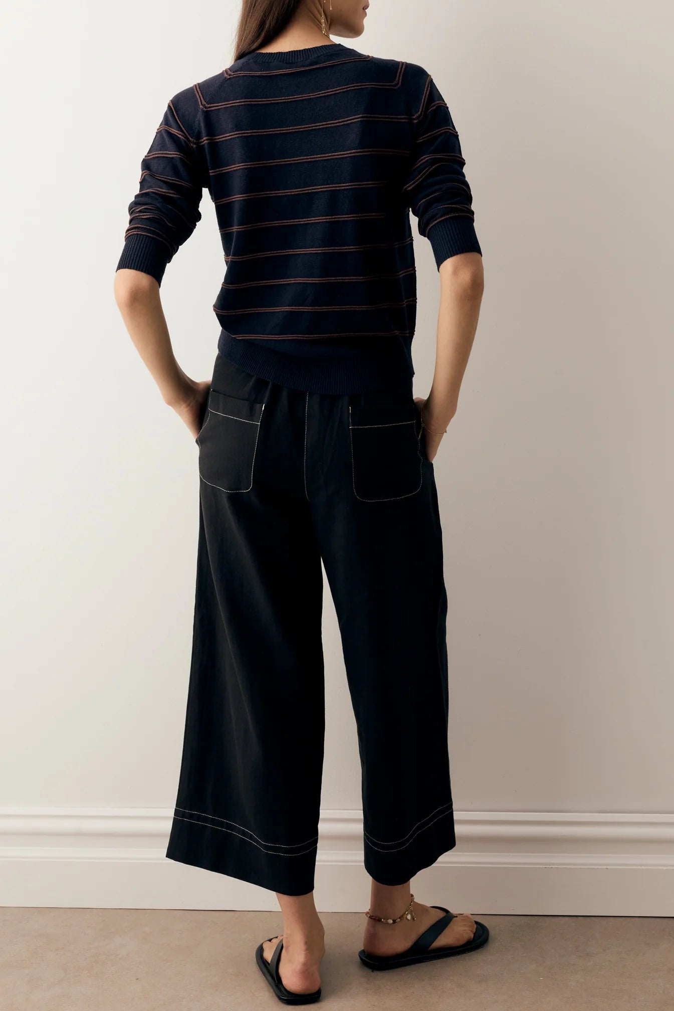 Person wearing a navy and chocolate striped top and black wide-leg pants against a plain background