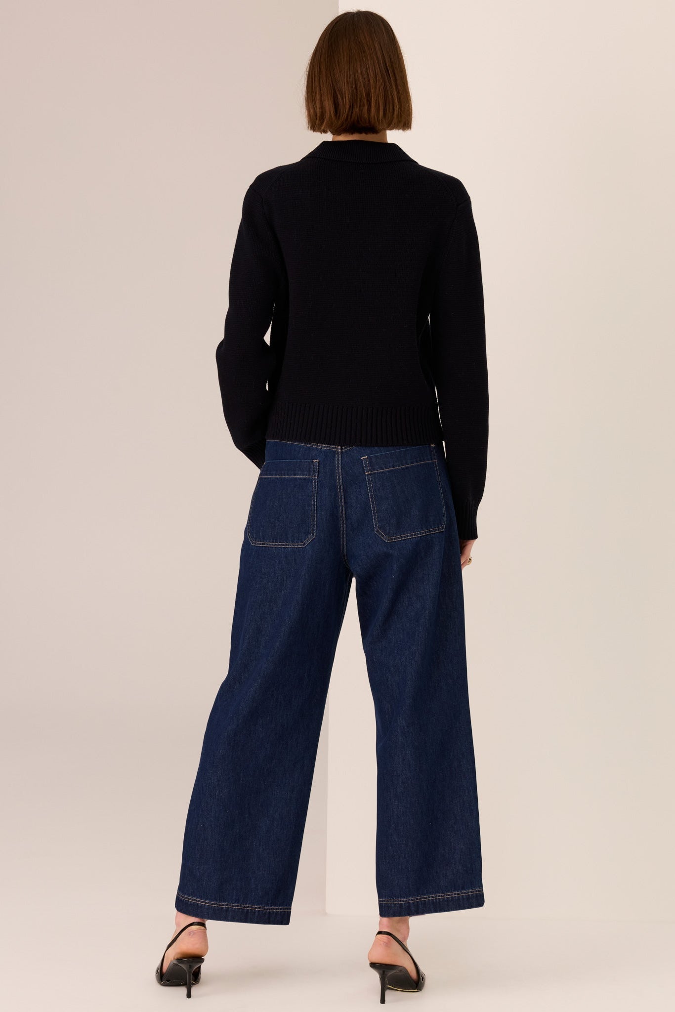Woman wearing a black sweater and dark blue jeans against a beige background