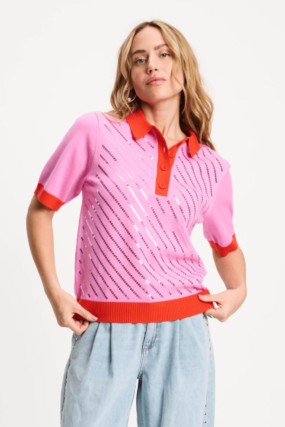 Woman wearing a pink and red polo shirt with light blue jeans on a white background