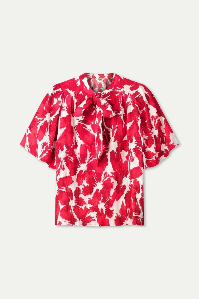 A short sleeve a red and white abstract floral print blouse with puff sleeves and a ruffled tie-neck, against a plain white background.