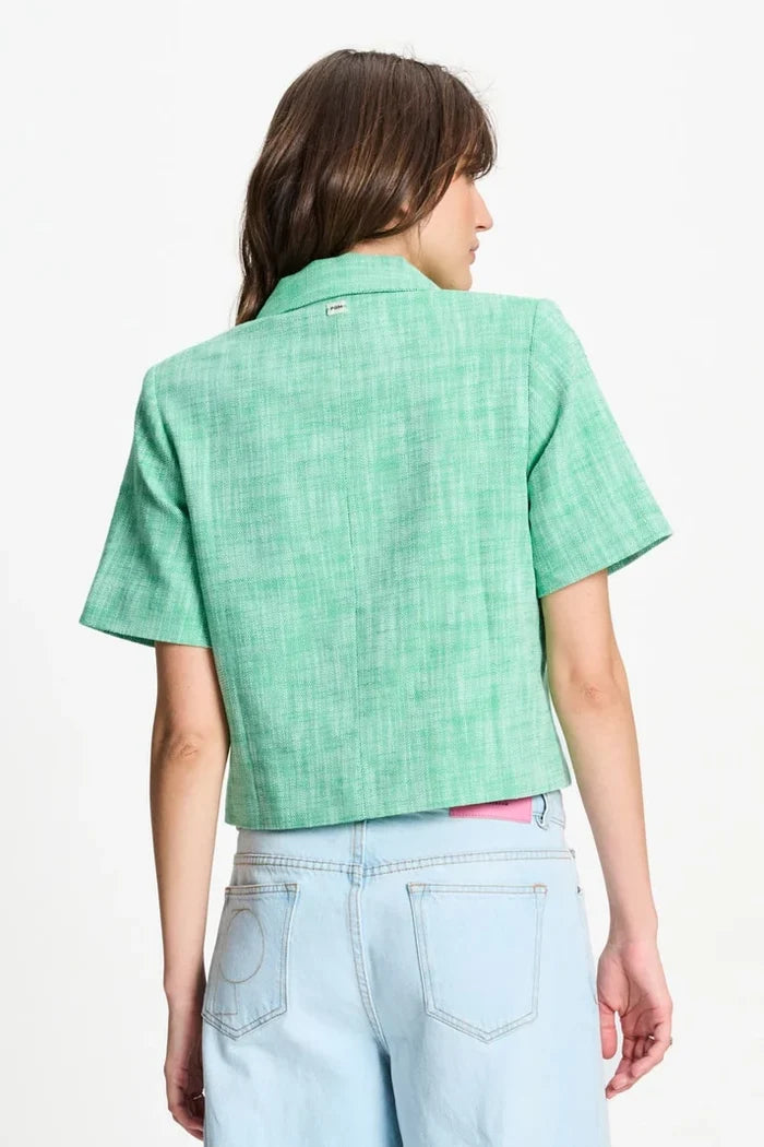 Woman shown from back wearing a green short sleeve cropped blazer and denim pants  on  a white background