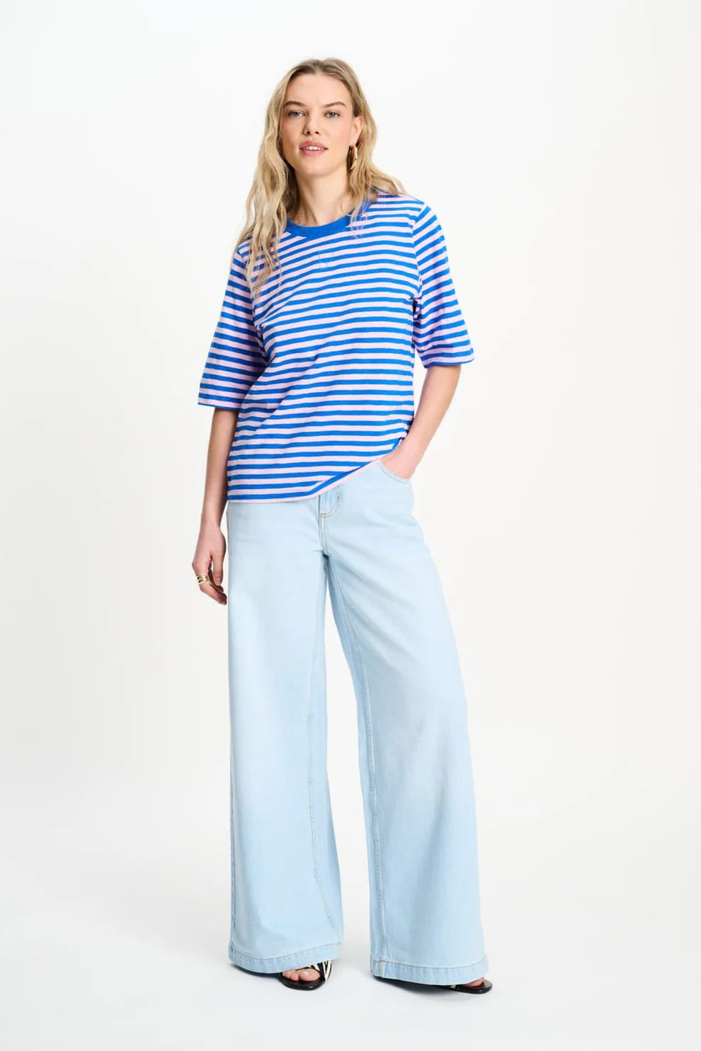 Woman wearing a blue and pink striped tee shirt and light blue jeans on a white background