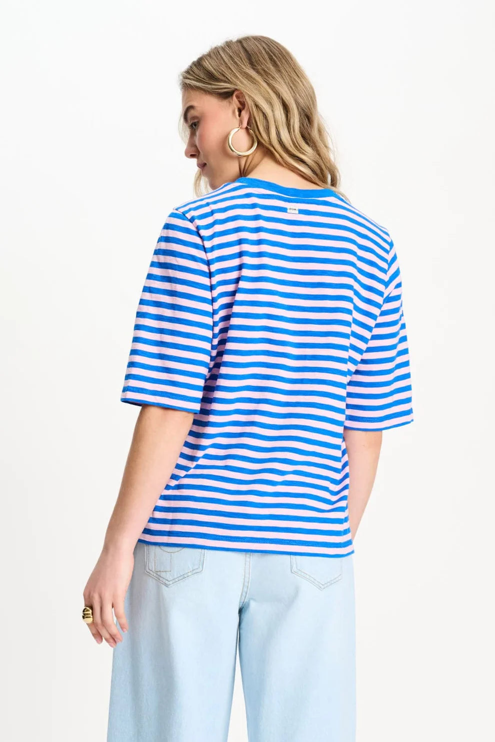A woman shown from the back wearing a blue and pink  horizontally striped short-sleeve t-shirt and light blue jeans against a plain white background.