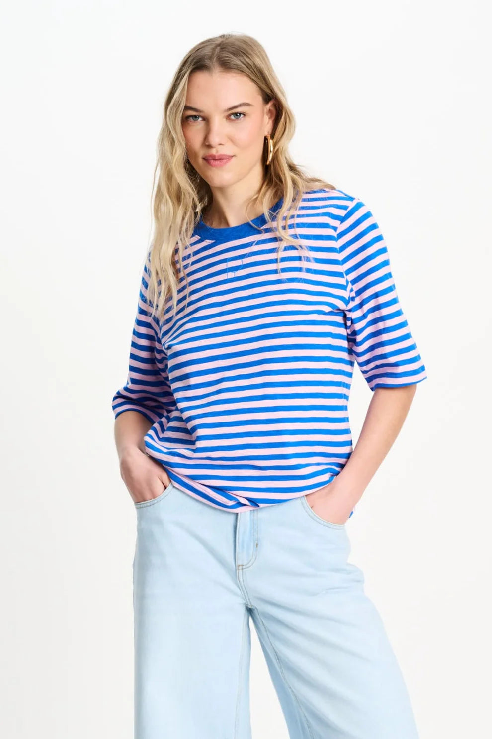 Woman wearing a blue and pink striped shirt with light blue jeans on a white background