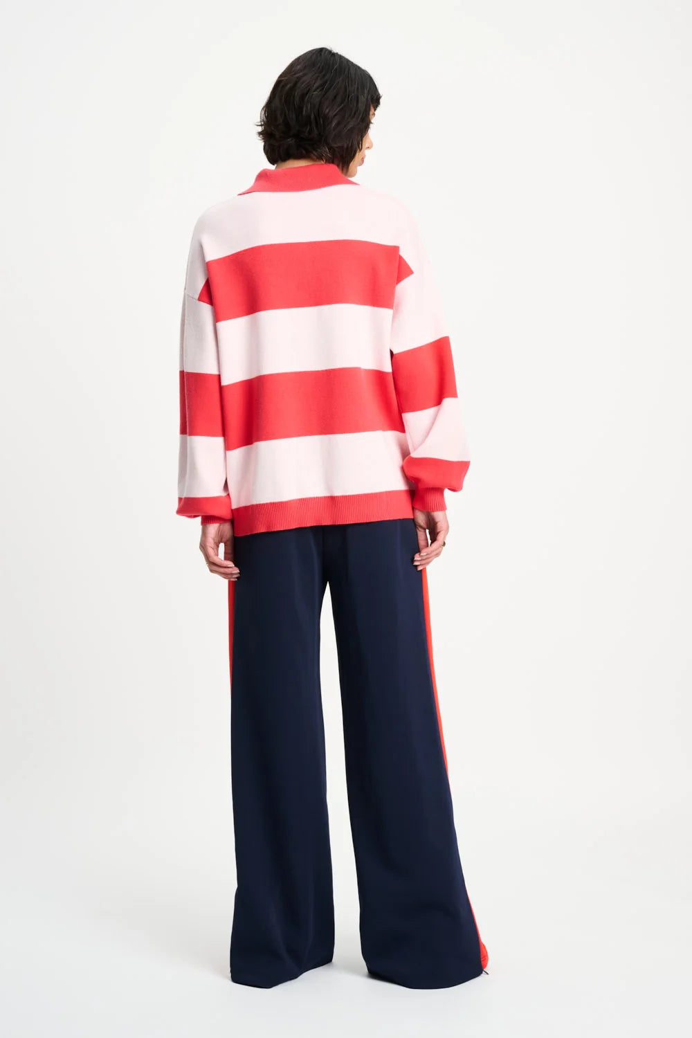 A model viewed from the back wearing a red and white horizontally striped long-sleeve top and navy wide-leg trousers with red side stripes, against a plain white studio background.