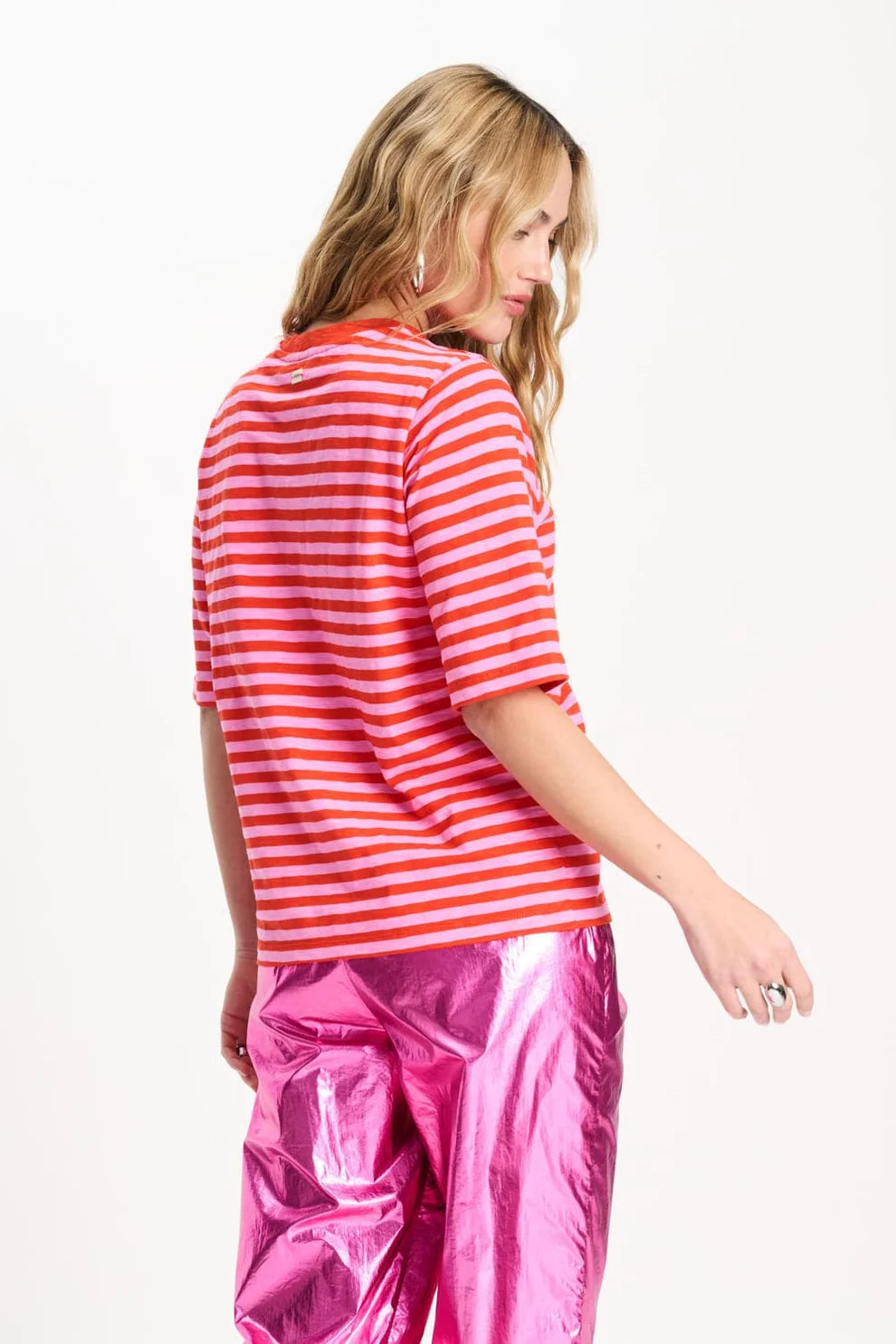 Woman wearing an orange and pink striped shirt and pink pants on a white background
