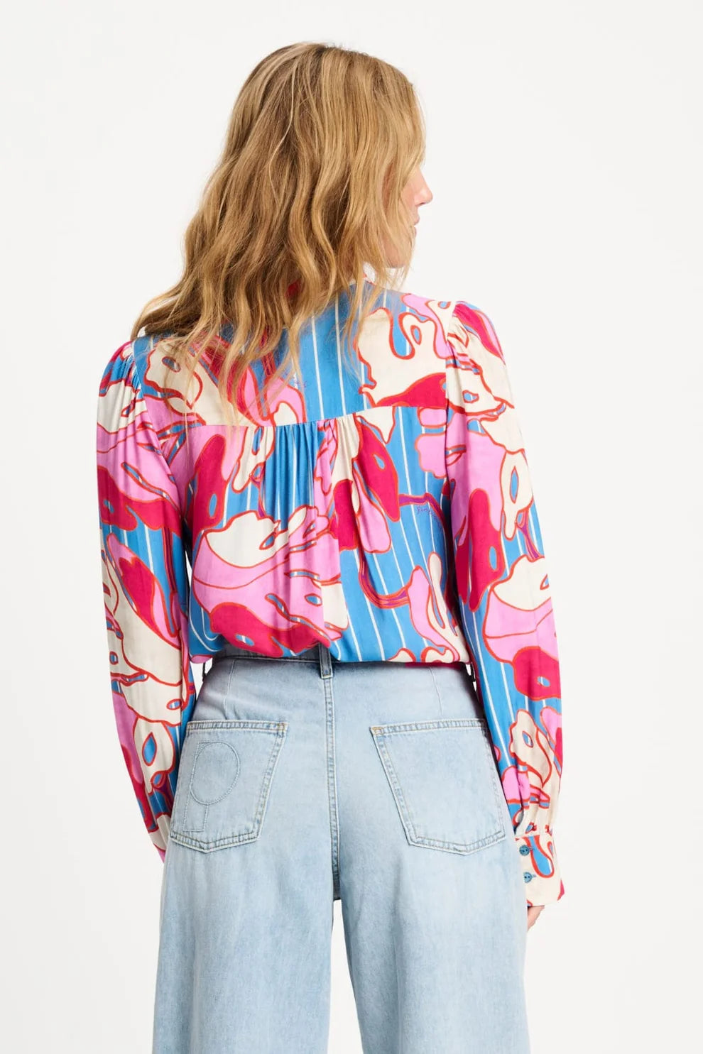 Women wearing a colourful floral blouse and light blue jeans on a white background showing back of shirt.  