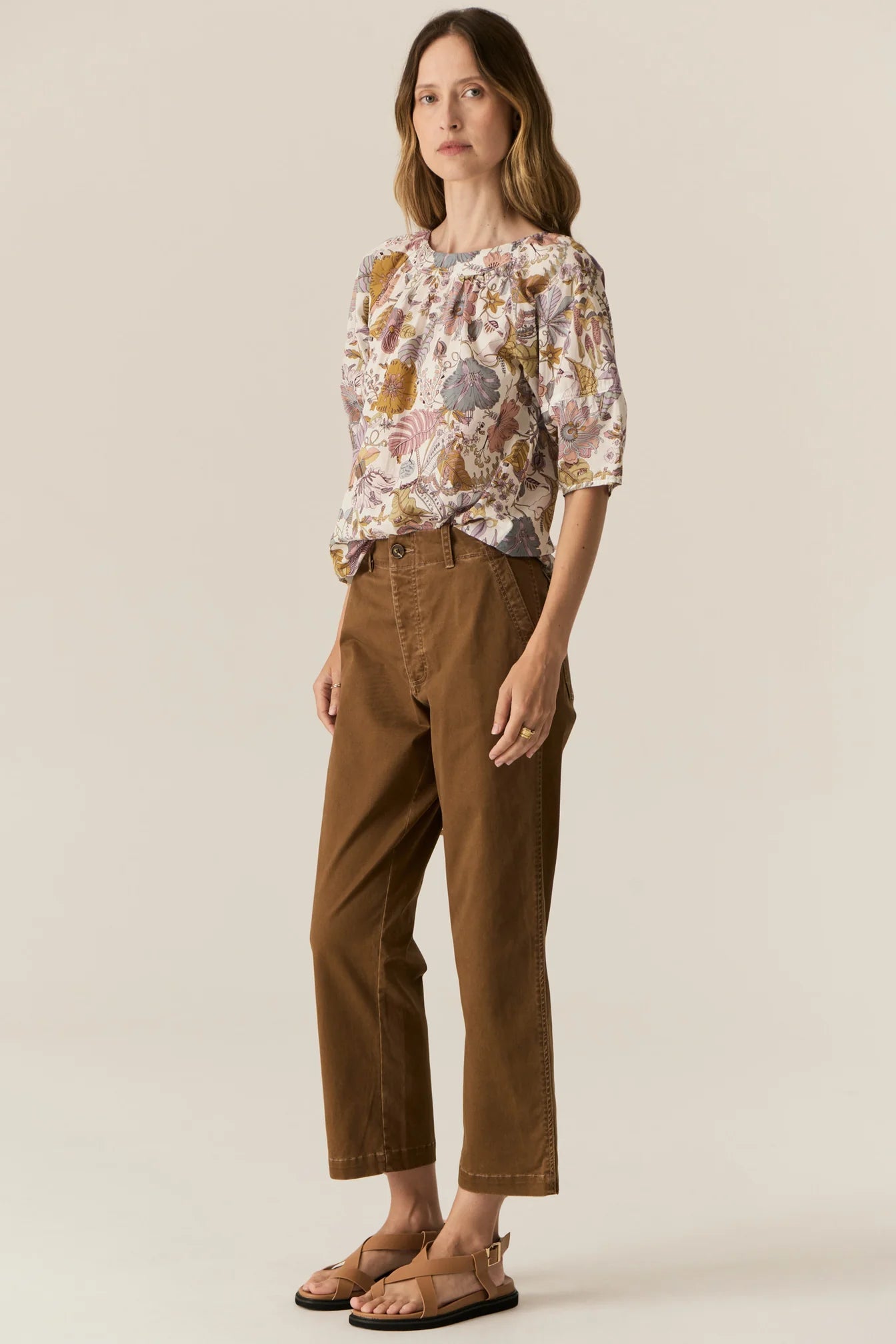 Woman wearing a short sleeve floral blouse and brown pants on a beige background