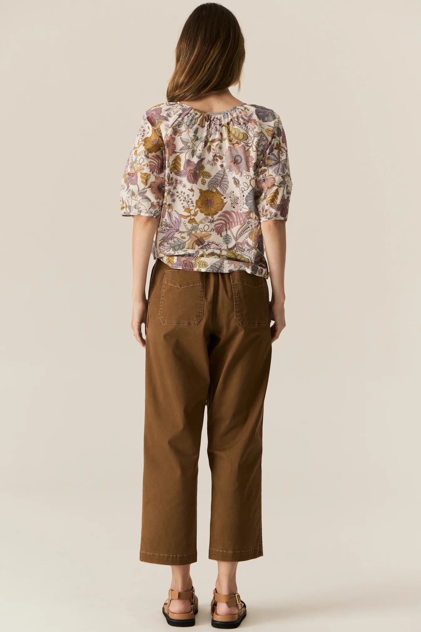 Woman wearing a short sleeve floral blouse and brown pants on a beige background