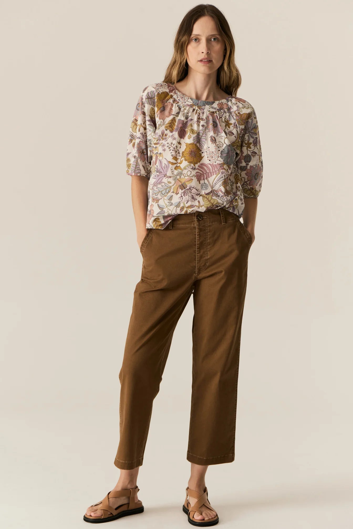 Woman wearing a short sleeve floral blouse and brown pants on a beige background