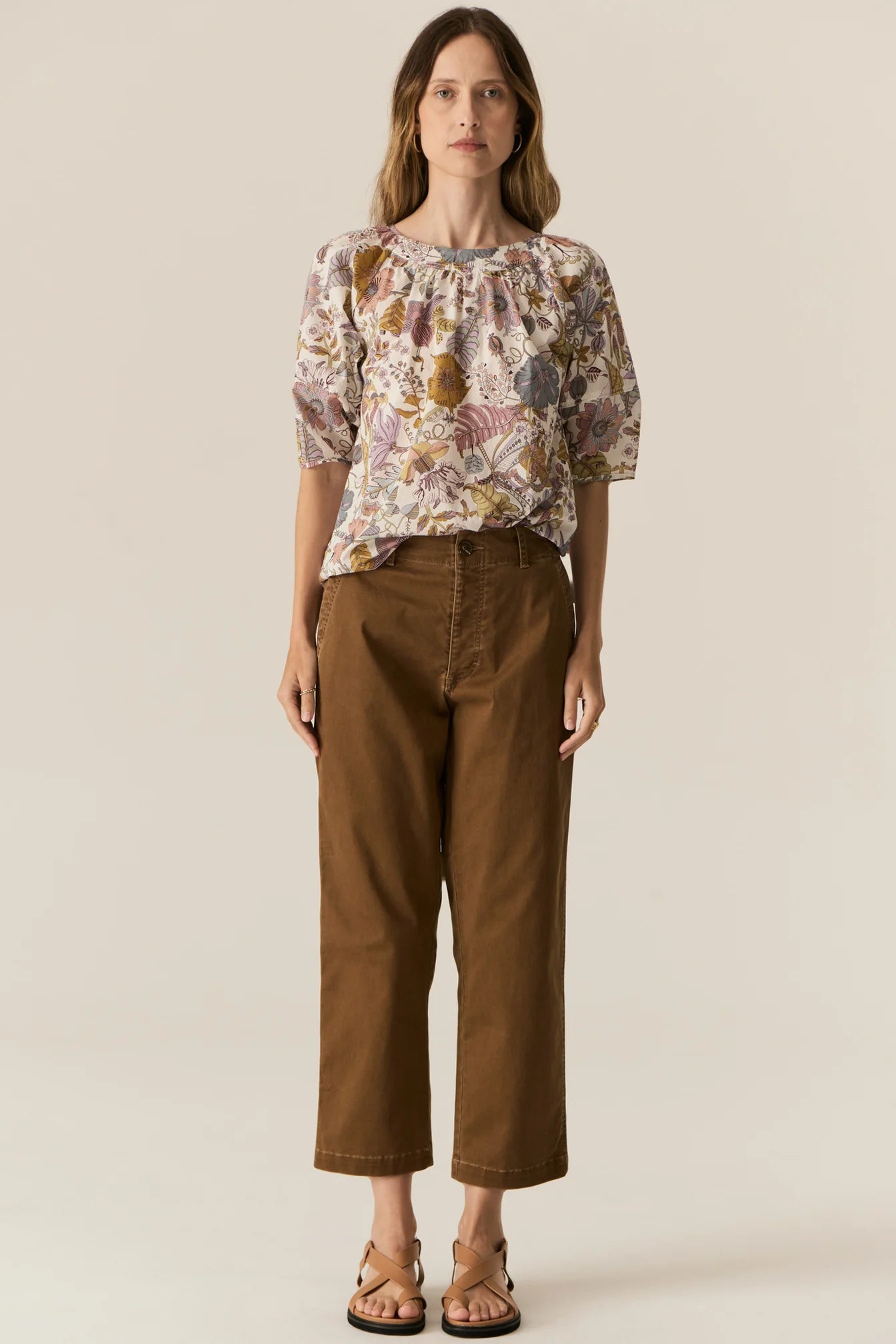 Woman wearing a short sleeve floral blouse and brown pants on a beige background