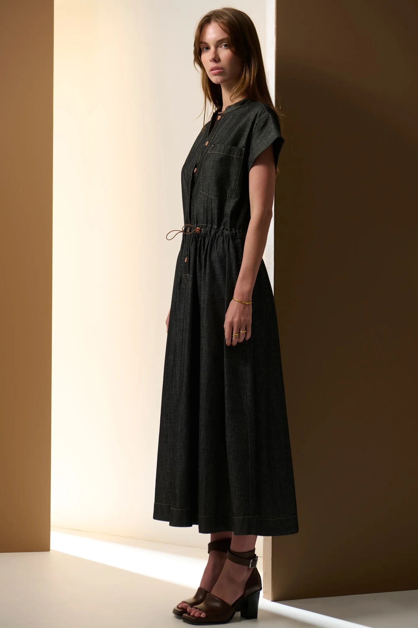 Woman wearing a black denim dress standing against a brown wall.