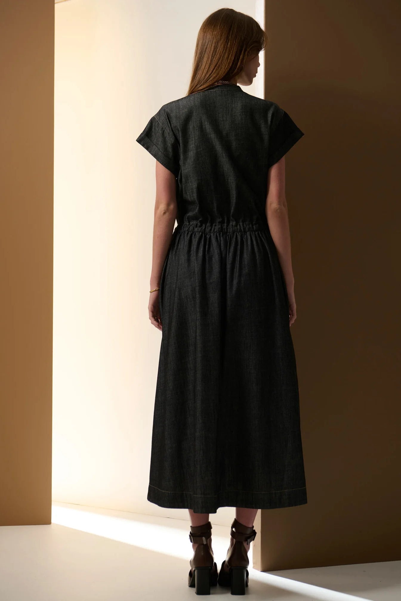 Woman wearing a black dress standing against a neutral wall.