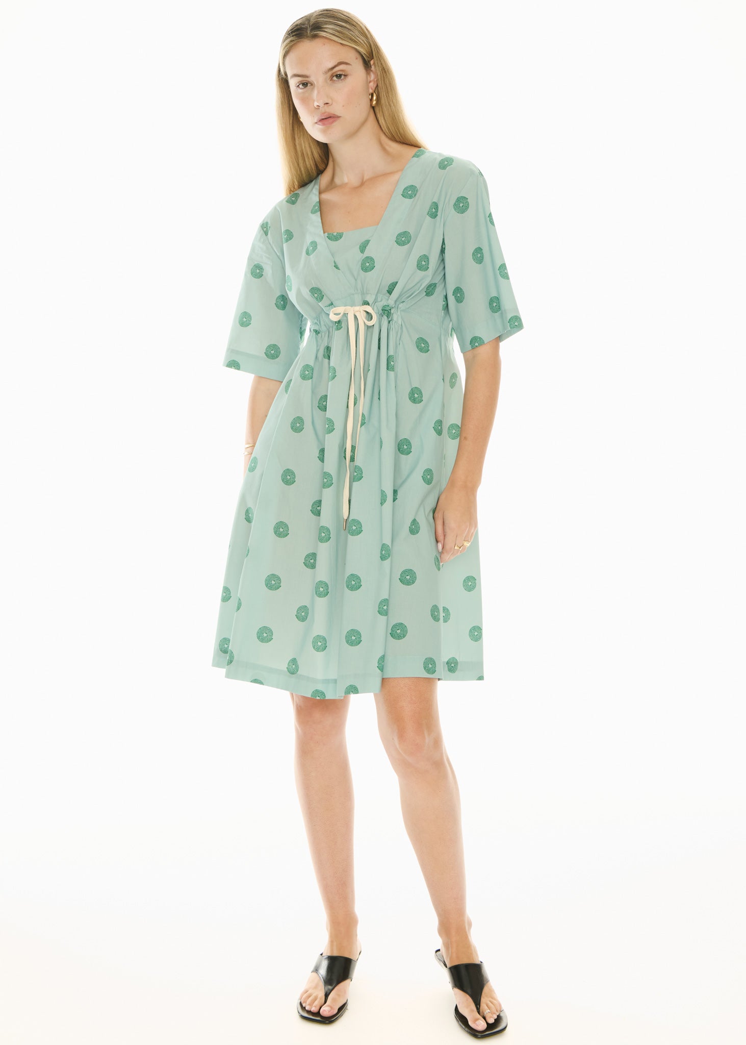 Woman wearing a green short sleeve midi patterned dress on a white background