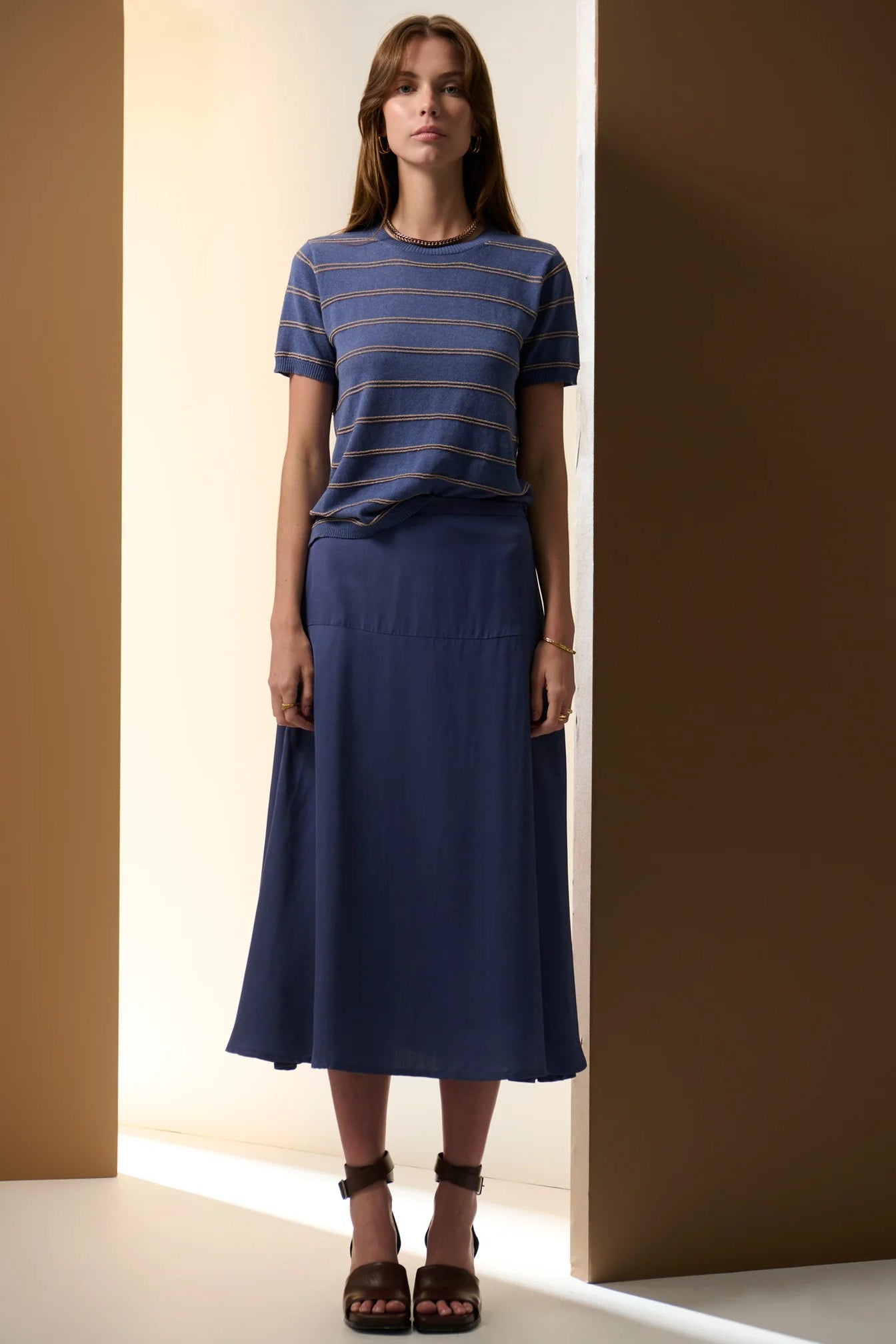 Woman wearing a blue striped shirt and navy skirt against a neutral background