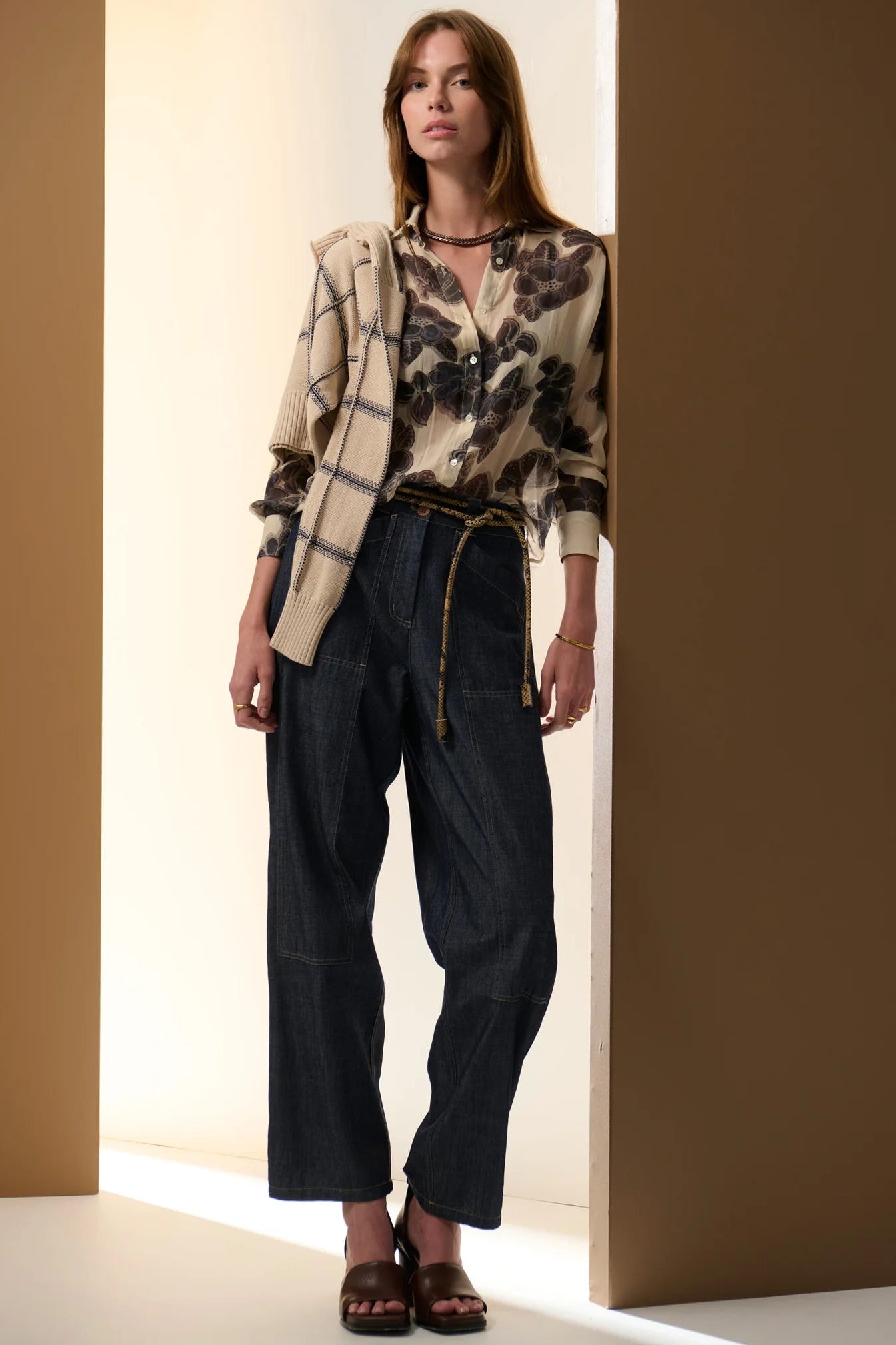 Woman wearing a floral shirt and dark denim wide leg pants standing against a neutral background