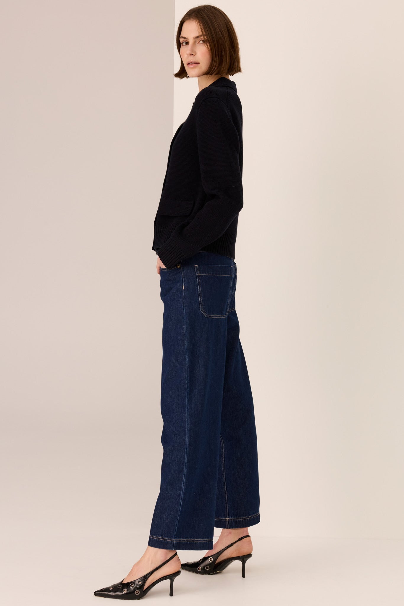 Woman wearing a black sweater and dark blue jeans against a beige background