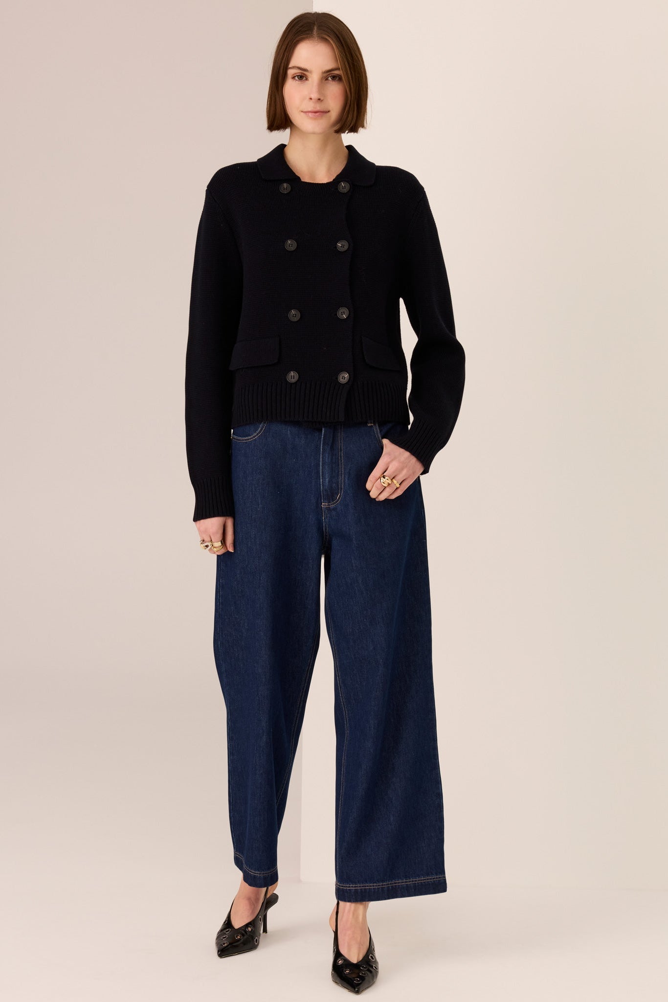 Woman wearing a black sweater and dark blue jeans against a beige background
