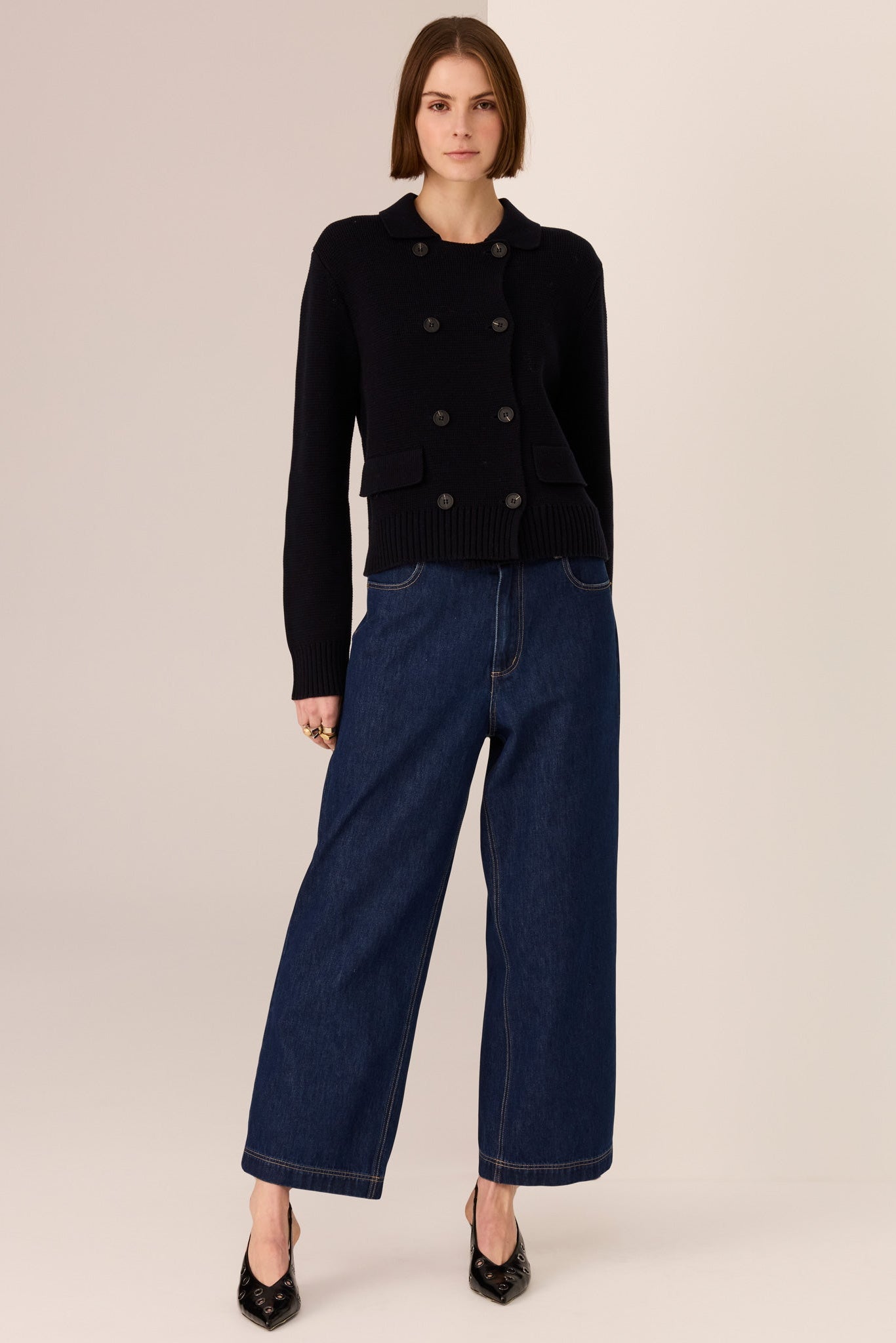 Woman wearing a black double breasted sweater and dark blue jeans against a beige background