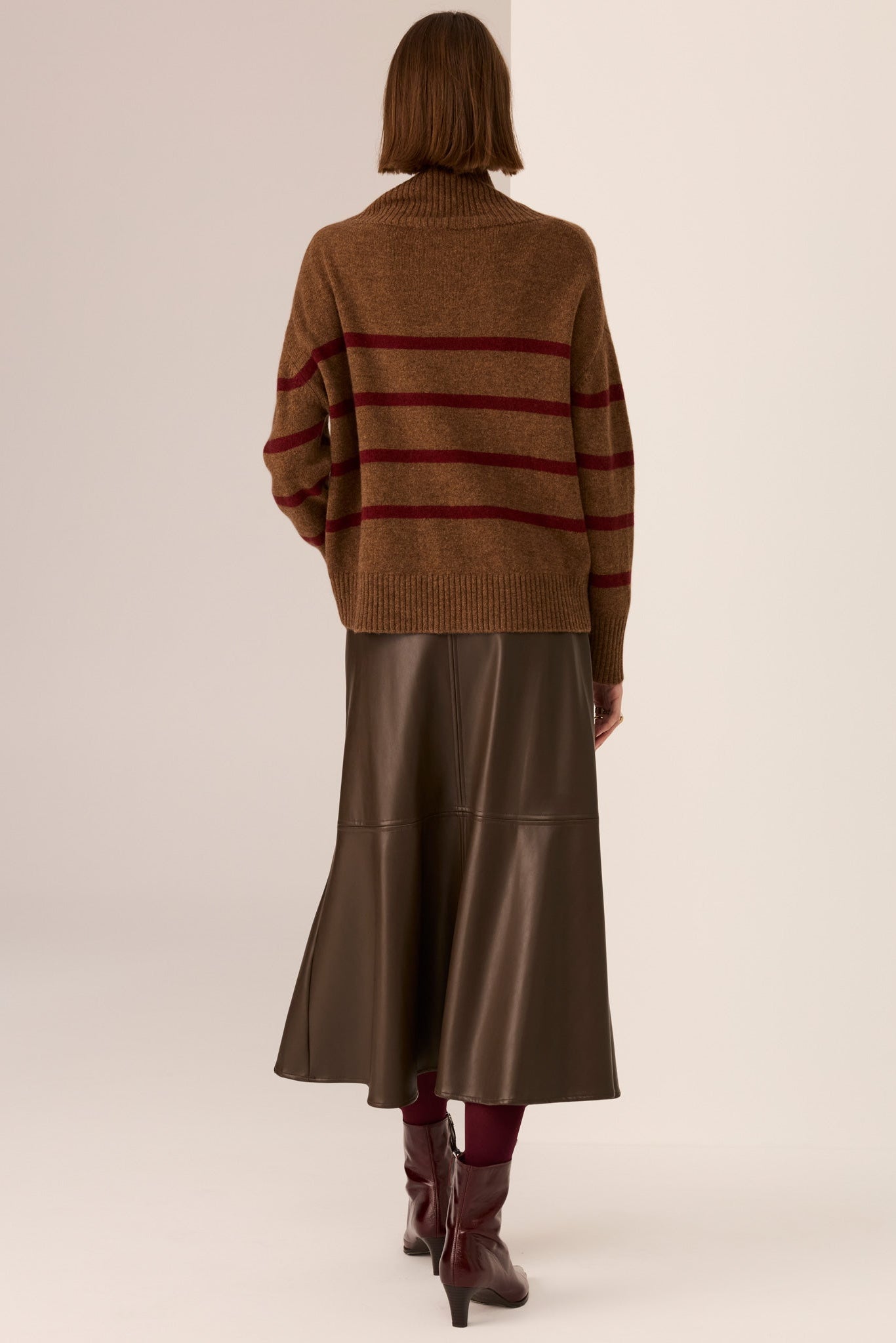 Person wearing a brown sweater with red stripes and a long brown skirt on a white background