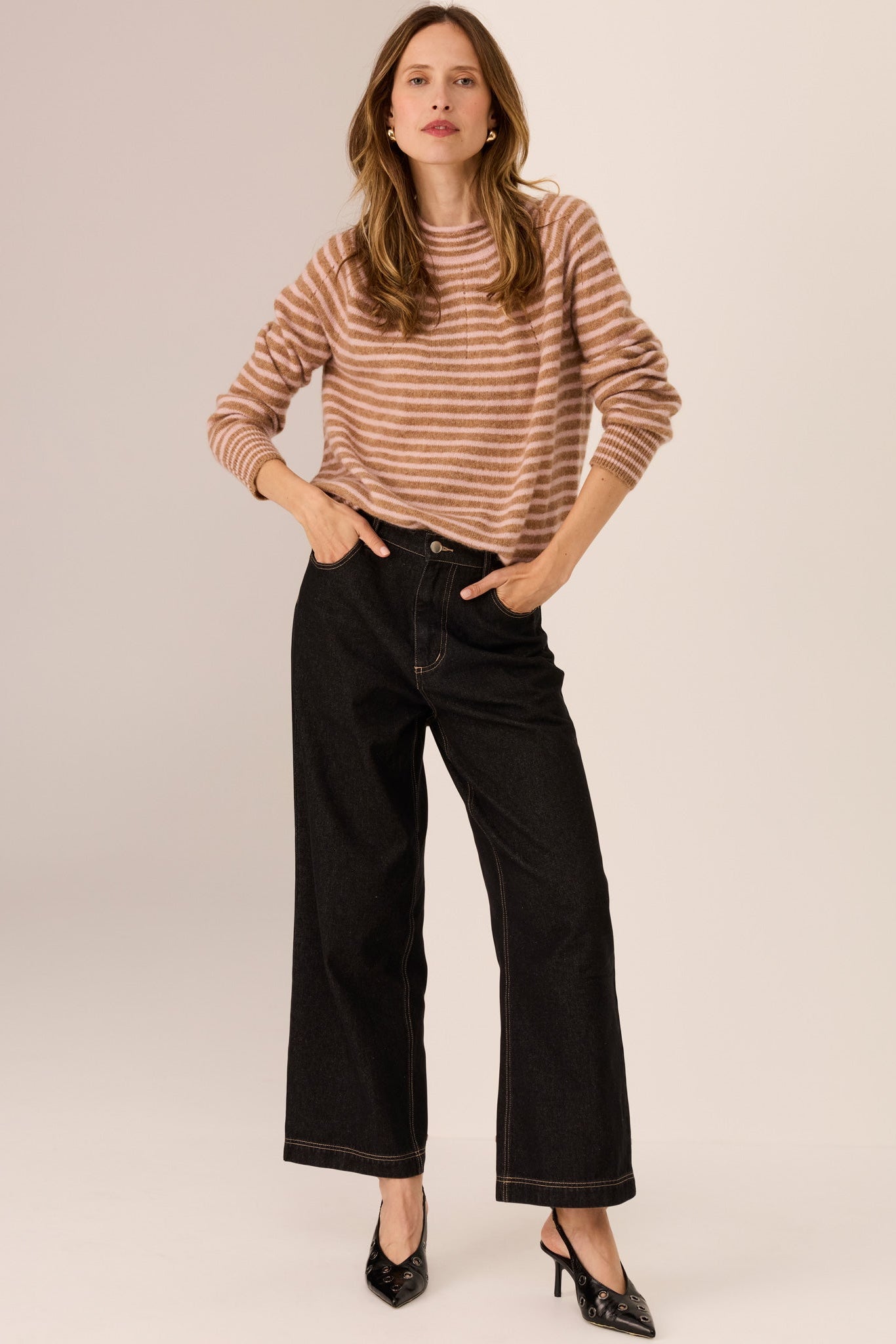 Woman wearing a camel and blush stripe long sleeve knit with wide leg dark denim jeans on a white background. 