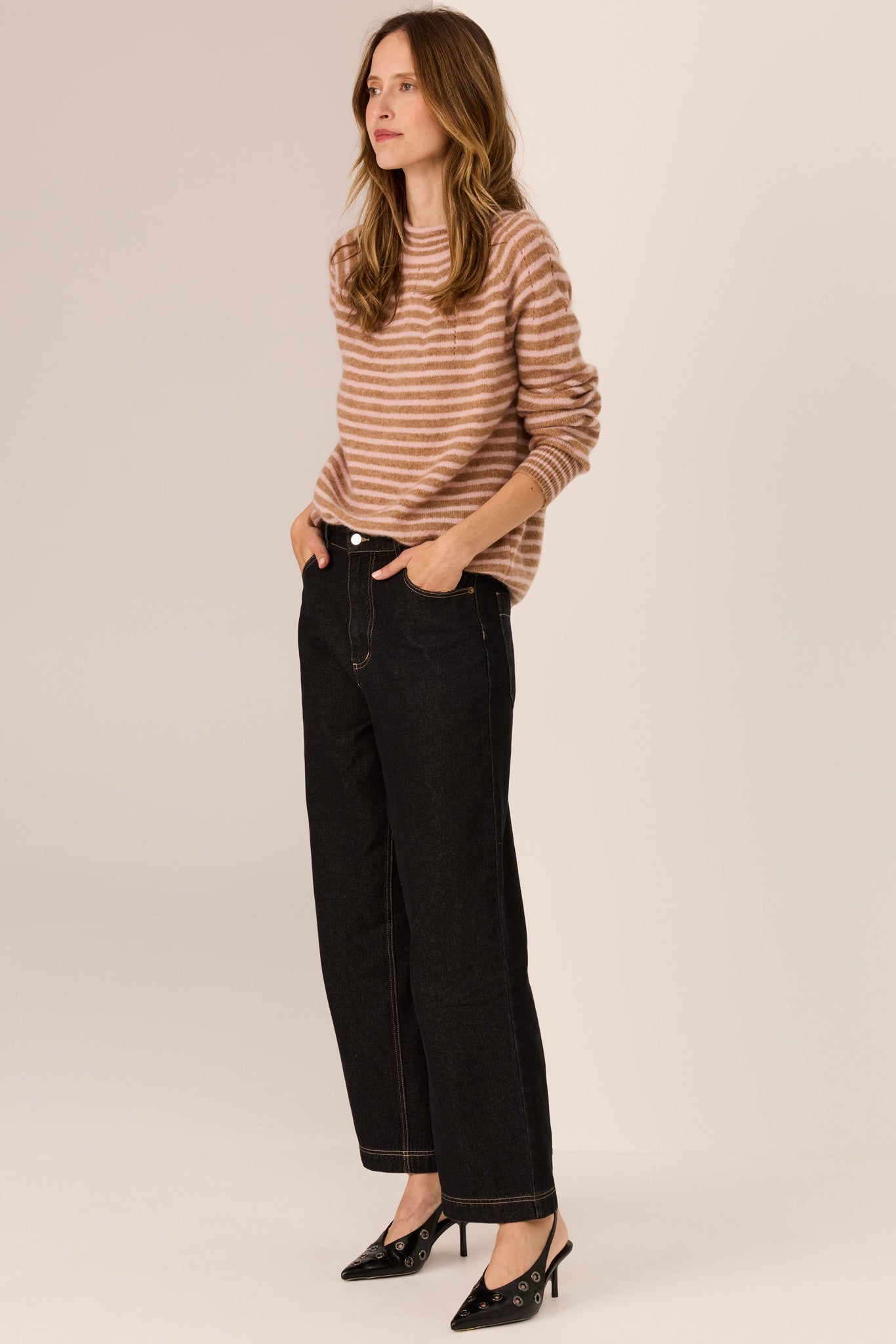 Woman wearing a camel and blush stripe long sleeve knit with wide leg dark denim jeans on a white background. 