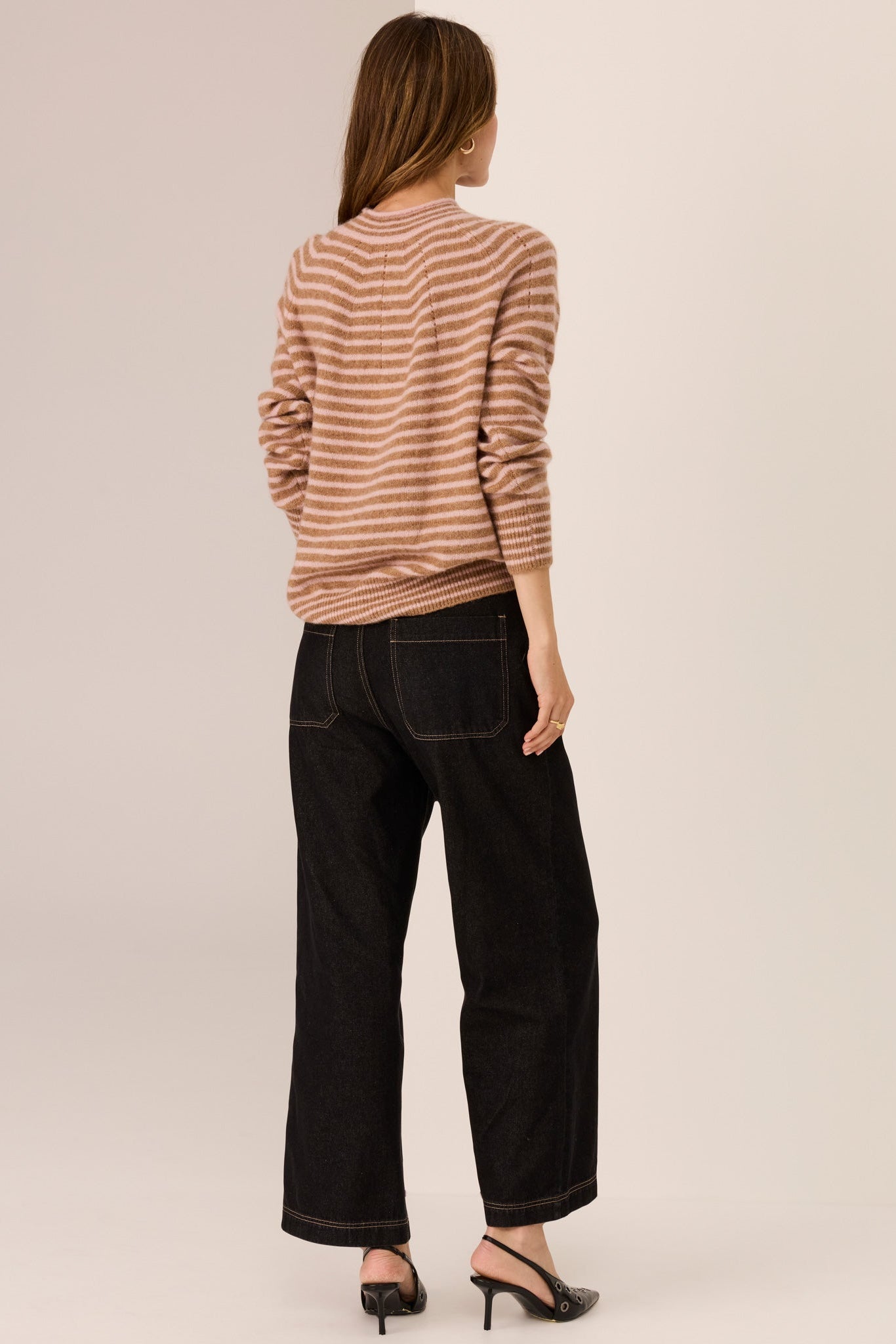 Woman wearing a camel and blush stripe long sleeve knit with wide leg dark denim jeans on a white background. 
