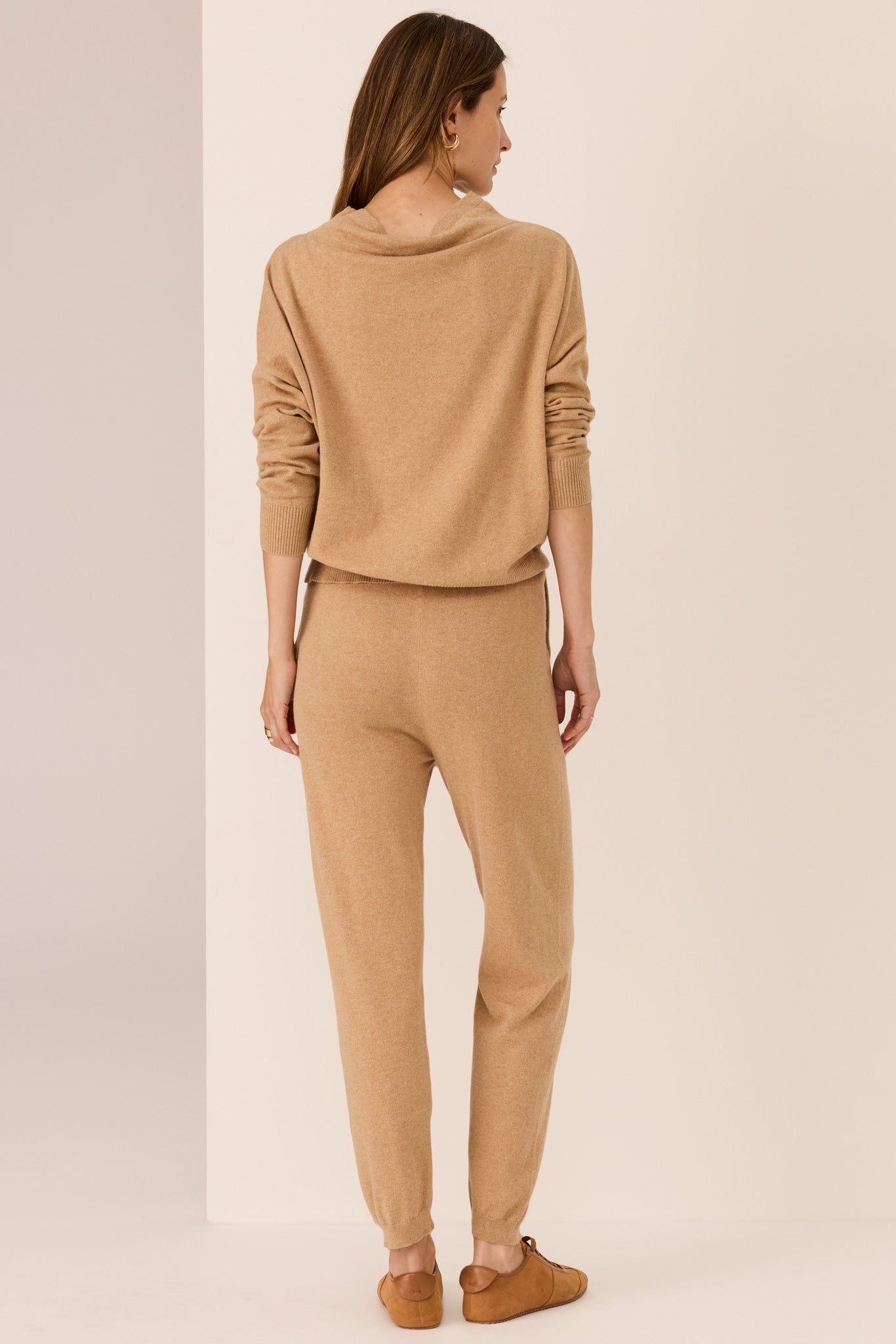 Woman wearing a beige sweater and matching pants on a plain background