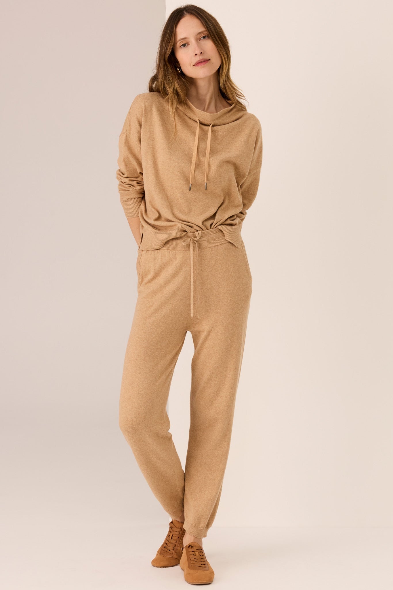 Woman wearing a beige sweater and matching pants on a plain background