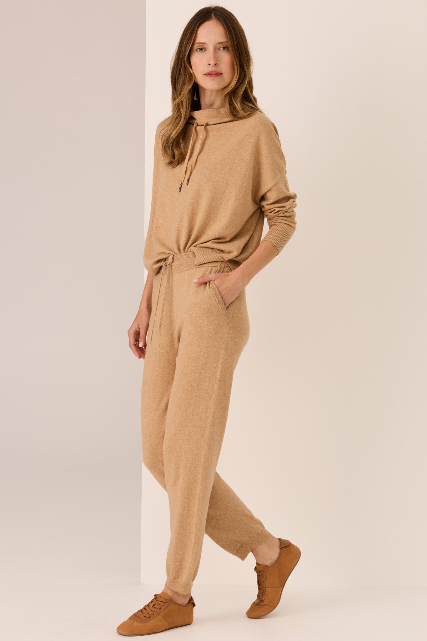 Woman wearing a beige sweater and matching pants on a plain background