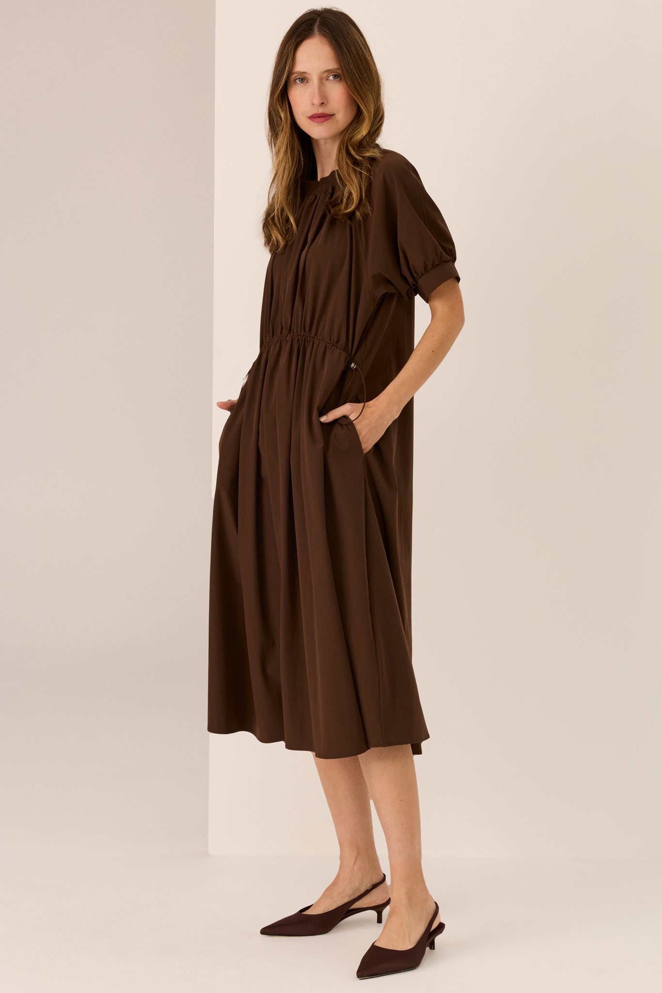 Woman wearing a Chocolate brown short sleeve dress with drop waist and draw cord on a white background. 

