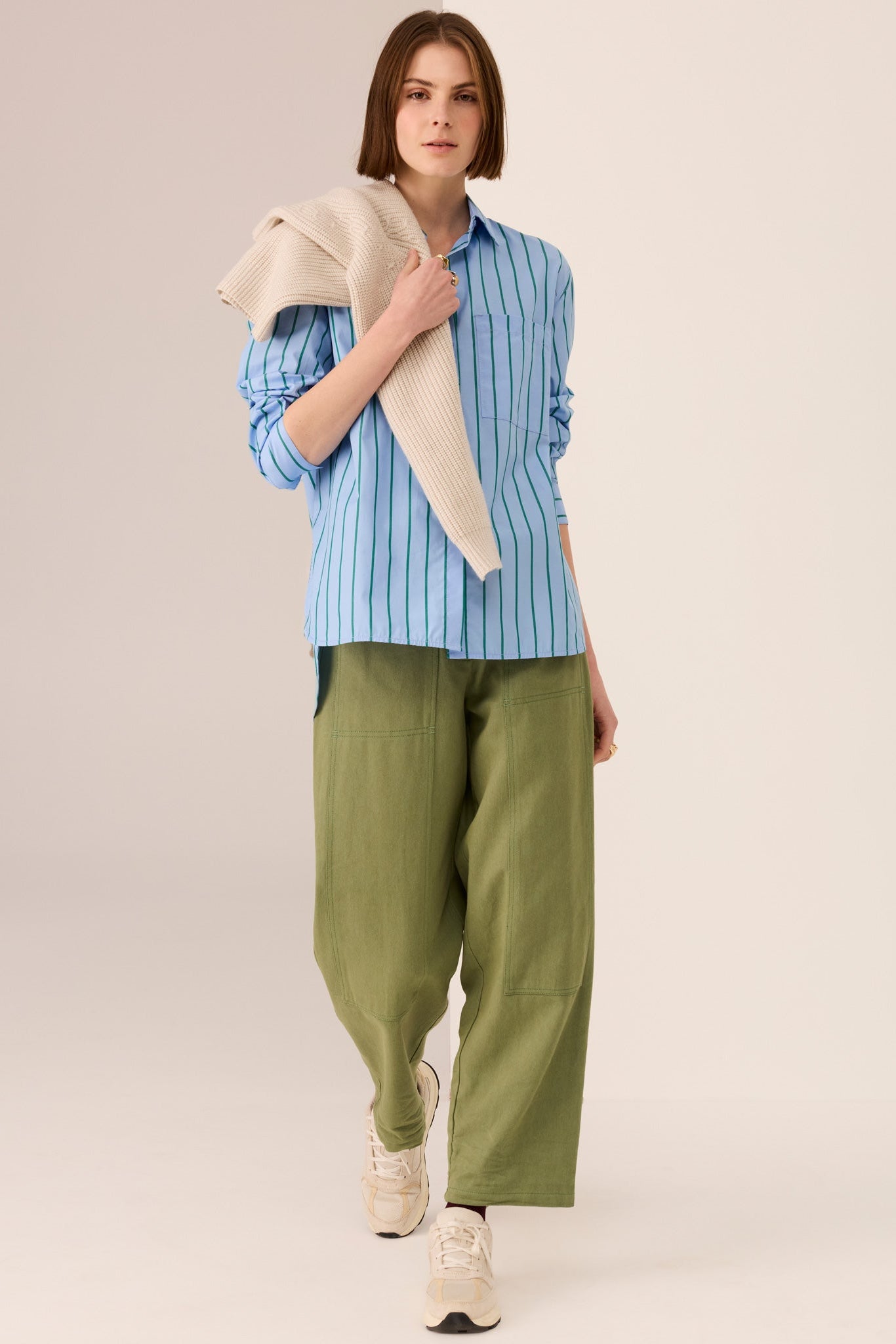 Woman wearing a blue shirt with green vertical stripe details and green pants on a white background. 