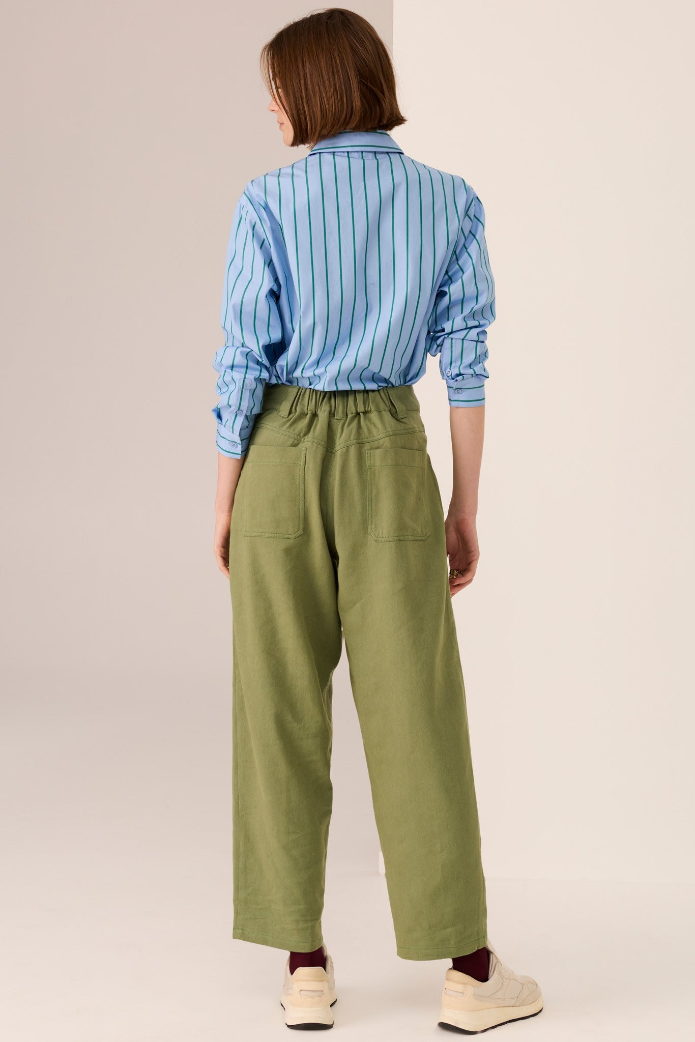 Woman wearing a blue shirt with green vertical stripe details and green pants on a white background. 