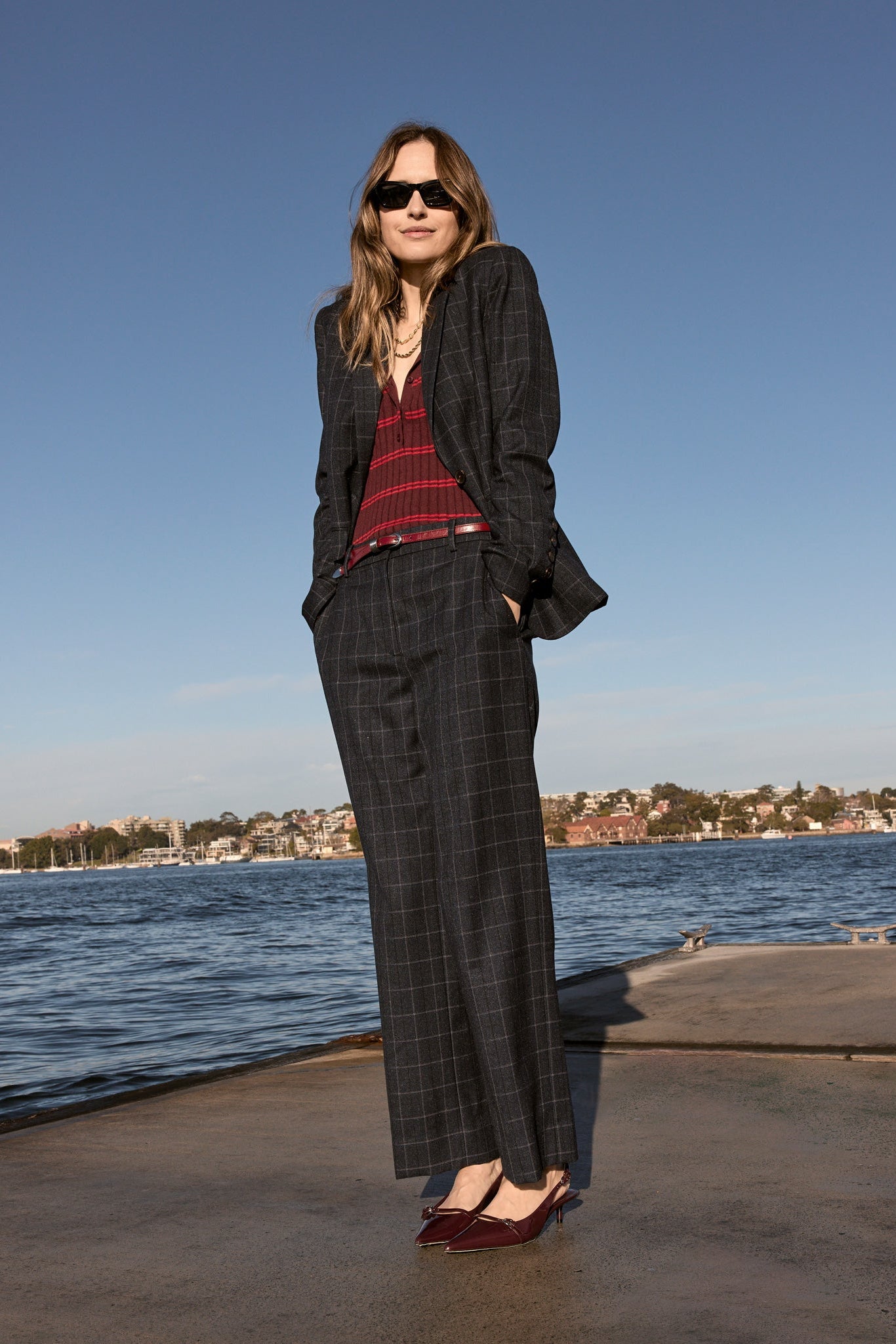 Woman wearing ink check suit blazer with matching pants and burgandy top underneath outside with ocean background. 
