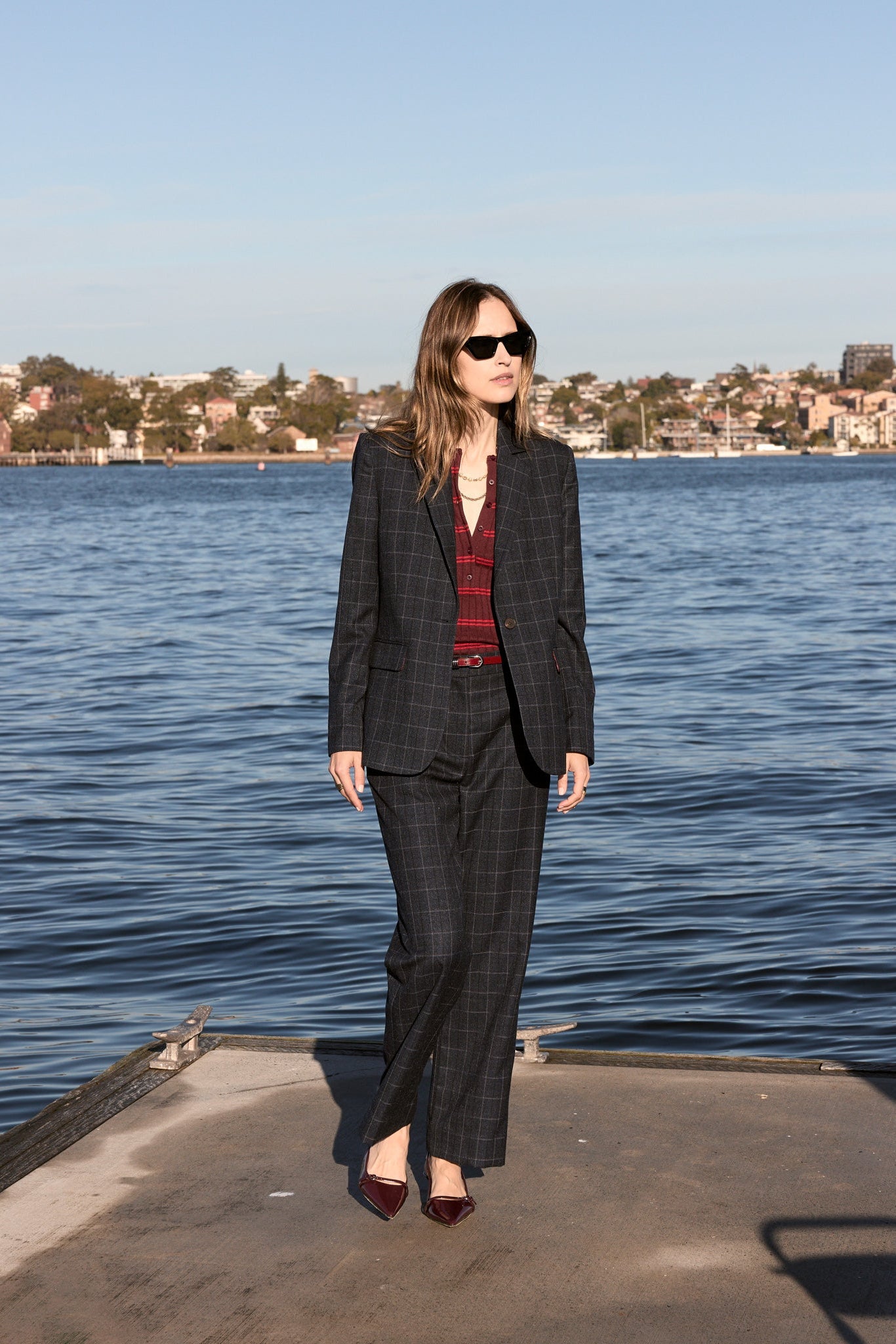 Woman wearing ink check suit blazer with matching pants and burgandy top underneath outside with ocean background. 
