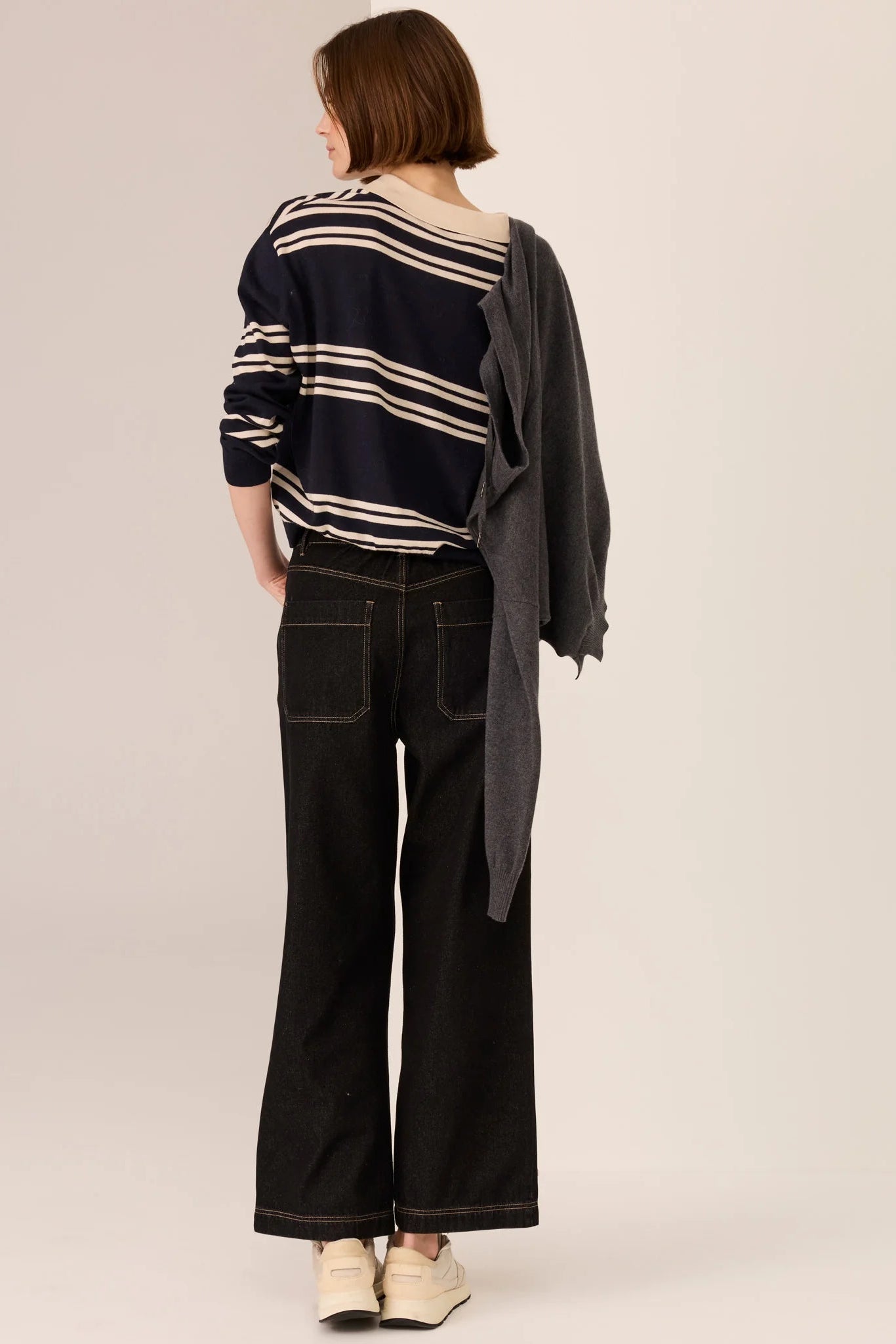 Person wearing a striped polo long sleeve sweater and black pants on a plain background